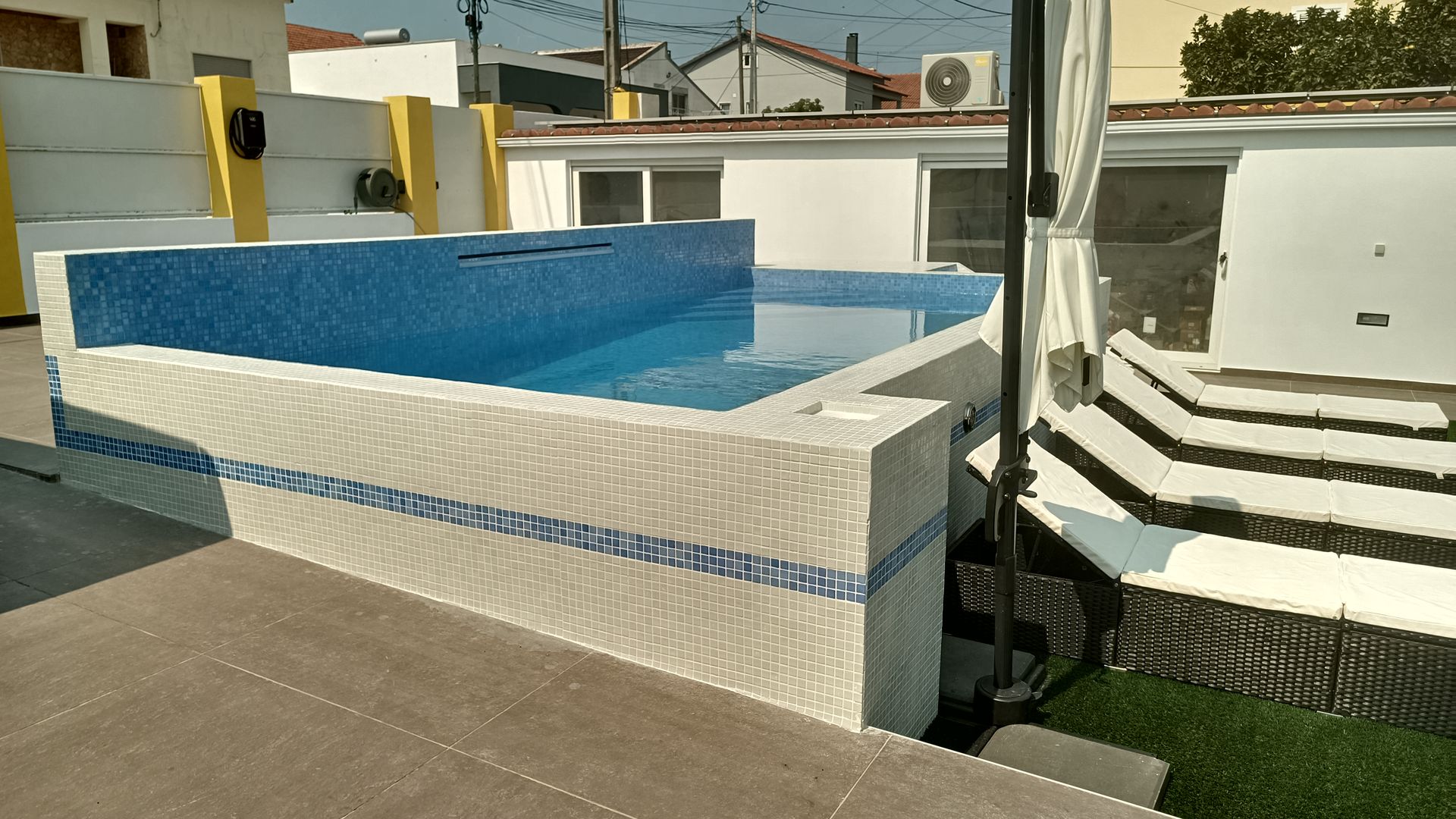 Uma pequena piscina revestida de azulejos em um terraço na cobertura, com água azul e cercada por azulejos brancos e azuis.