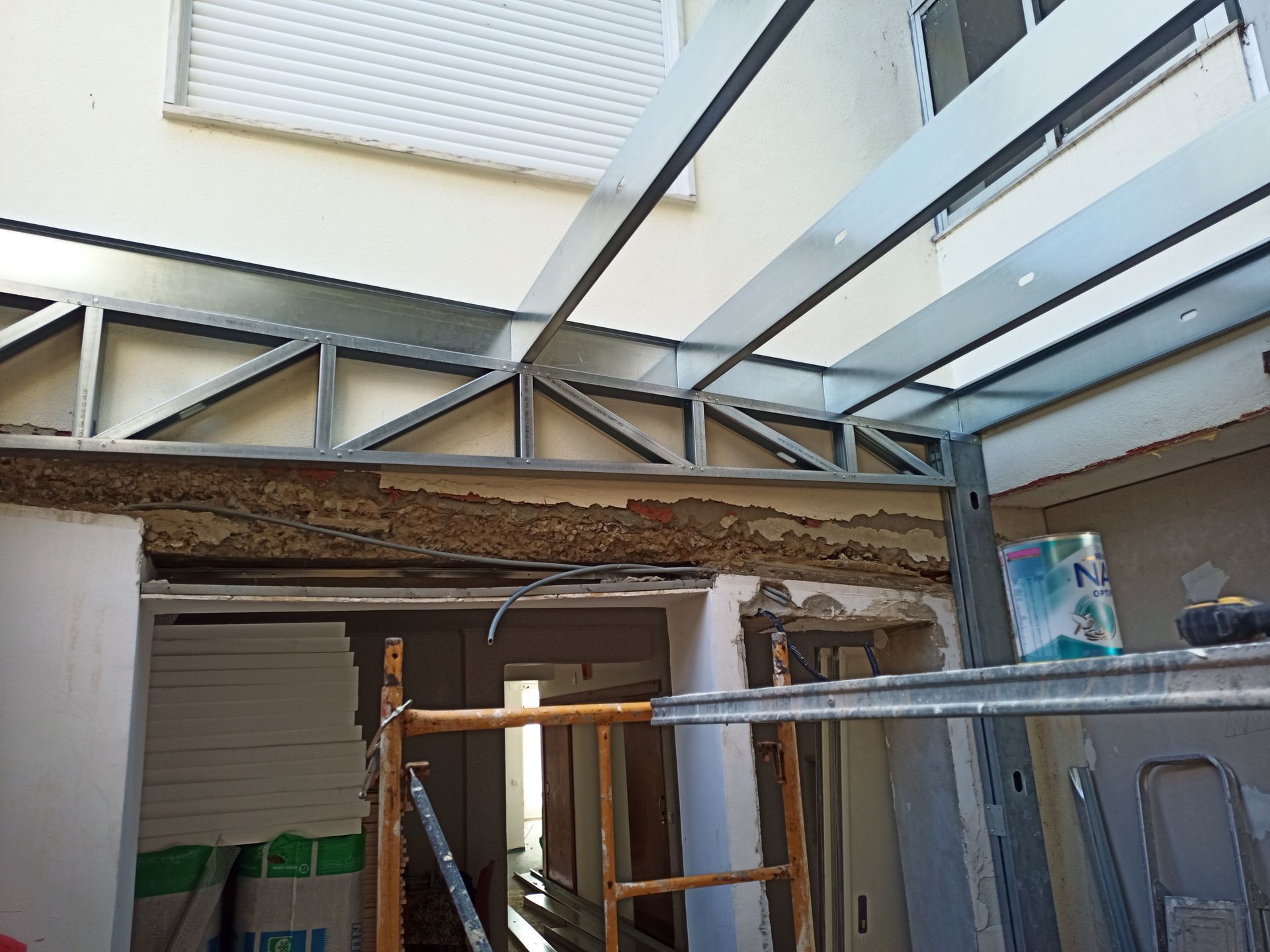 Canteiro de obras: estrutura metálica para uma extensão do telhado, cobrindo uma entrada. As paredes estão parcialmente acabadas.