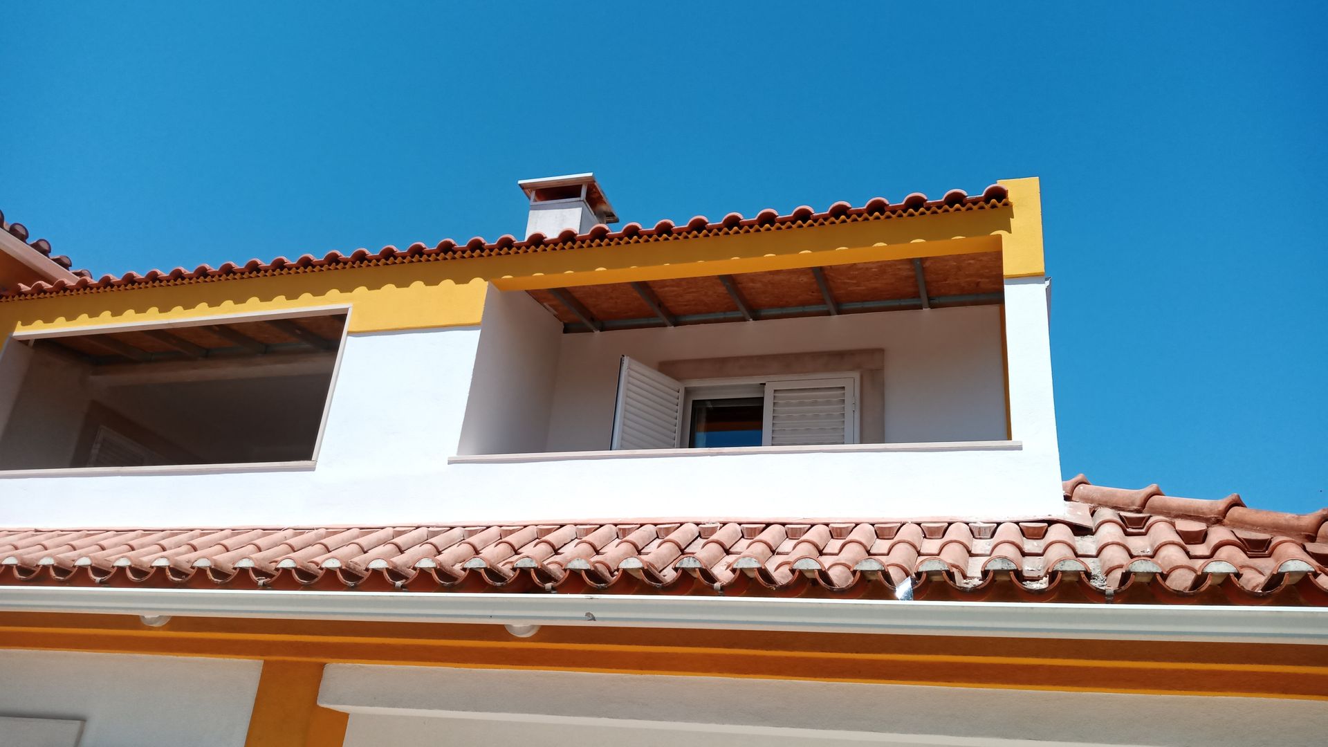 Prédio branco com telhado de telhas laranja e detalhes em amarelo contra um céu azul brilhante.