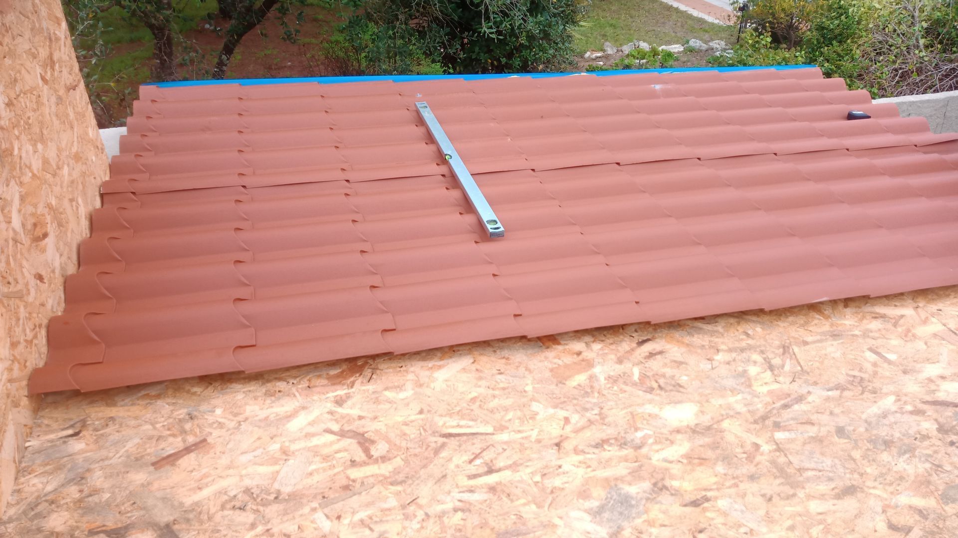 Painéis de telhado ondulados vermelhos colocados sobre uma superfície de OSB (painel de madeira orientada), nivelados.