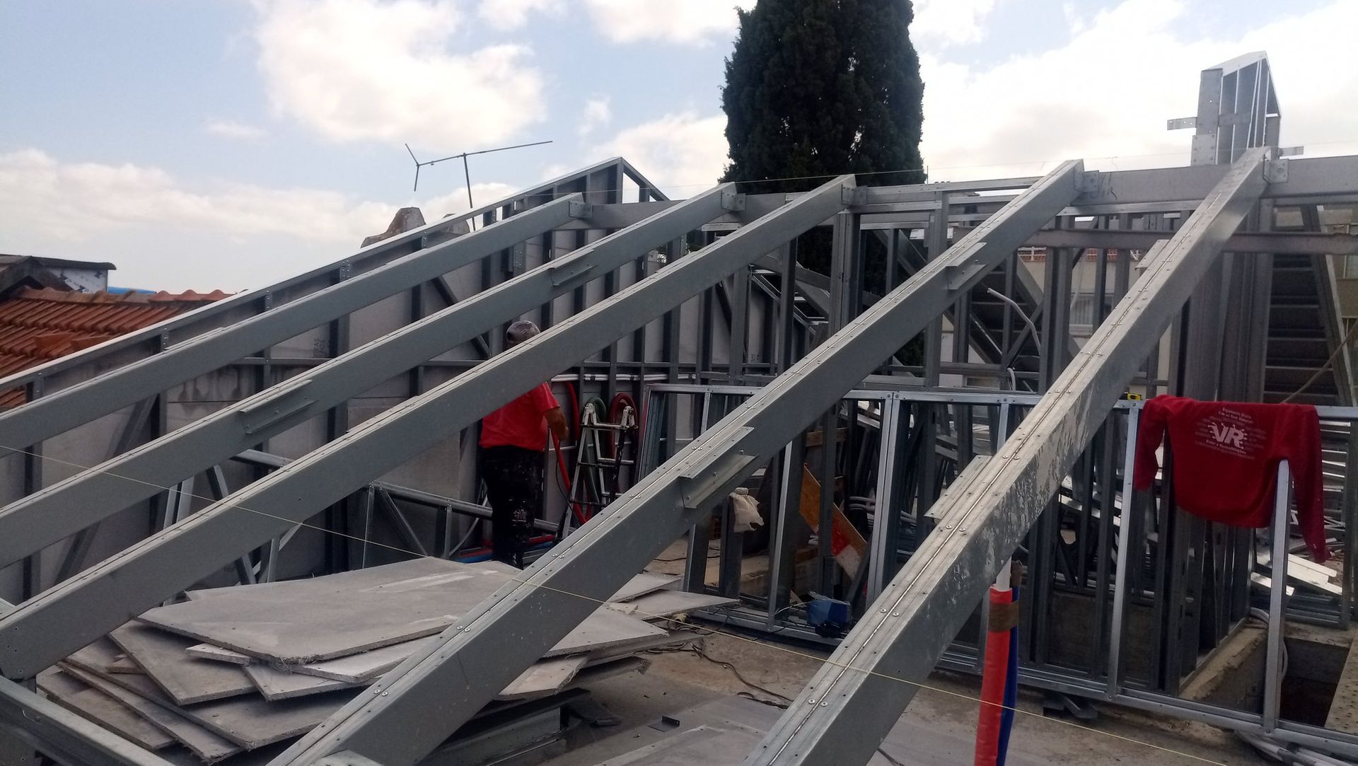 Estrutura metálica sobre um telhado com uma pessoa vestindo uma camisa vermelha.