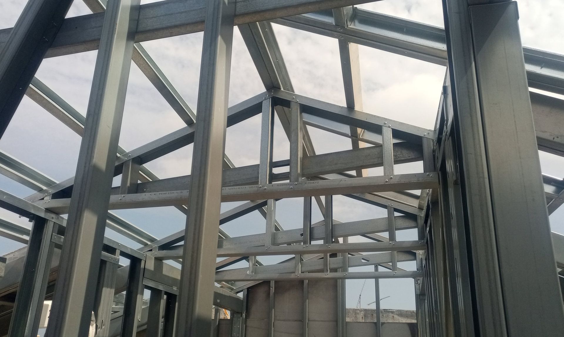 Estrutura metálica de um edifício com telhado inclinado sob um céu nublado.