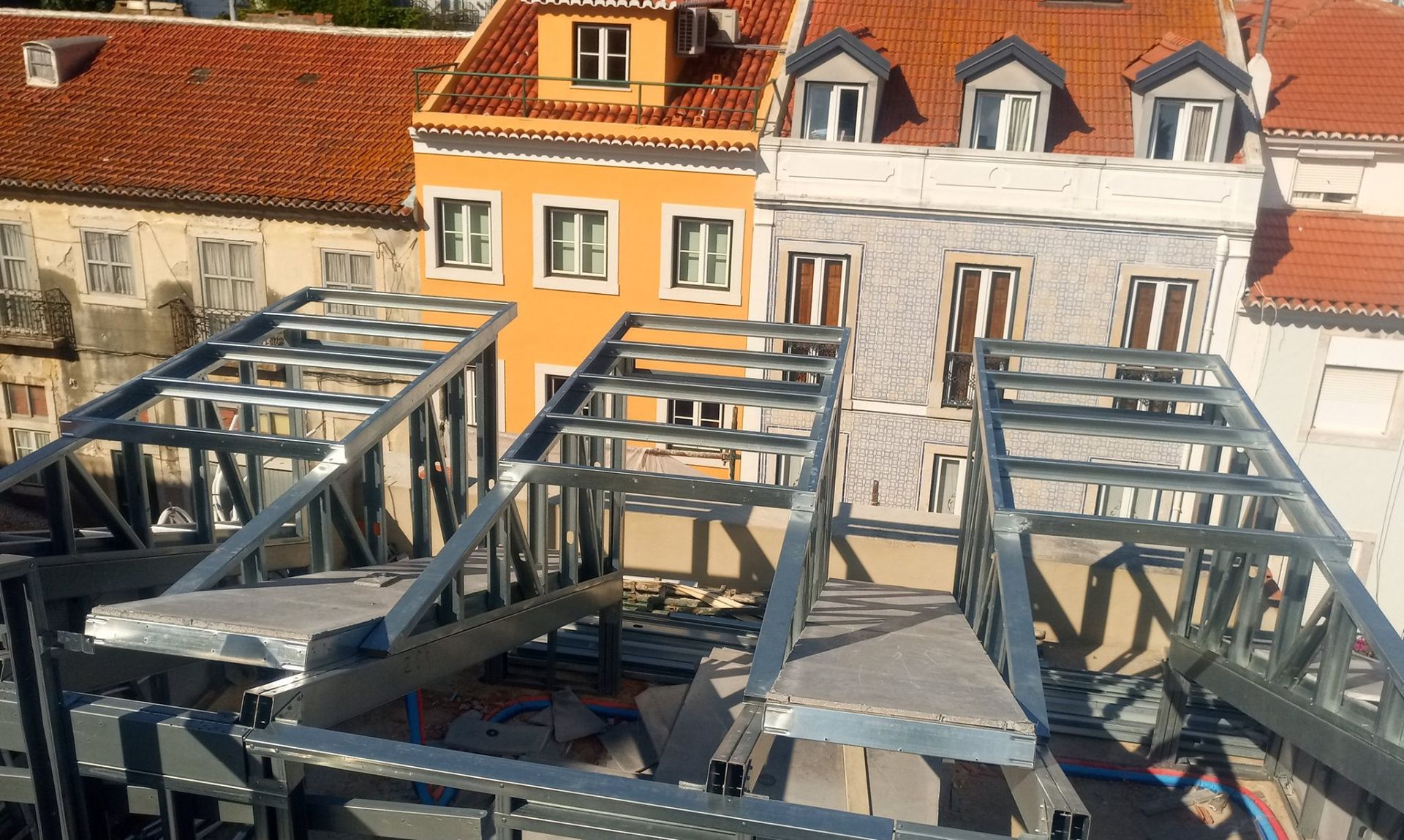 Estrutura de aço em um telhado com prédios coloridos ao fundo.