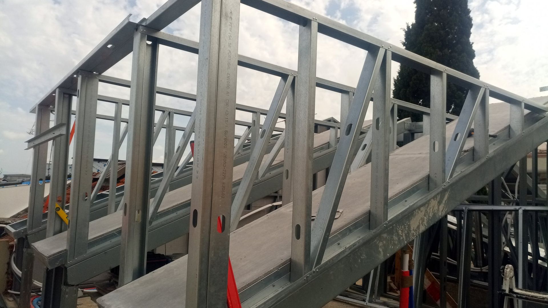 Estrutura metálica de uma escada em construção, com travessas e piso cinza na passarela.