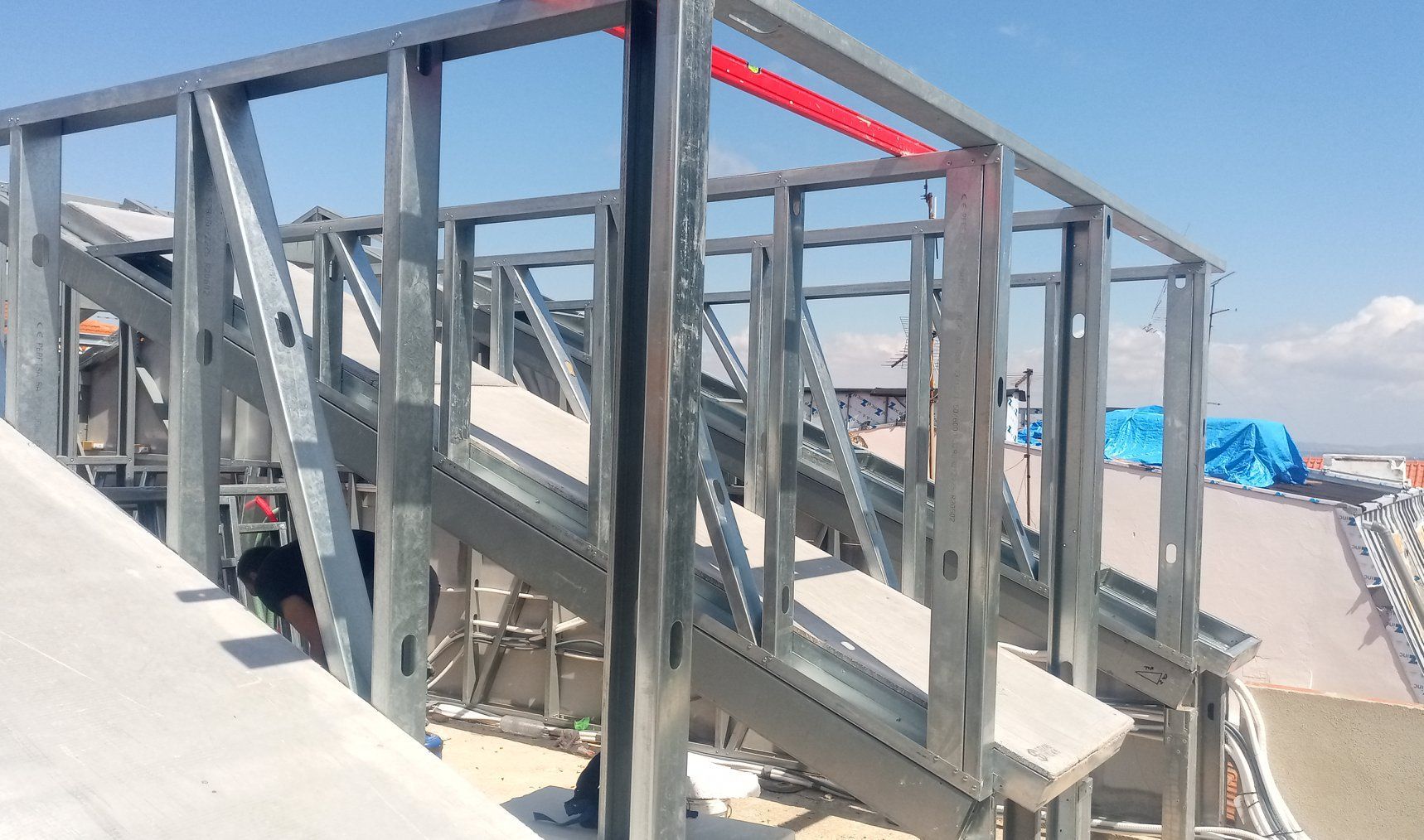 Estrutura metálica de uma escada em construção com um céu azul claro ao fundo.