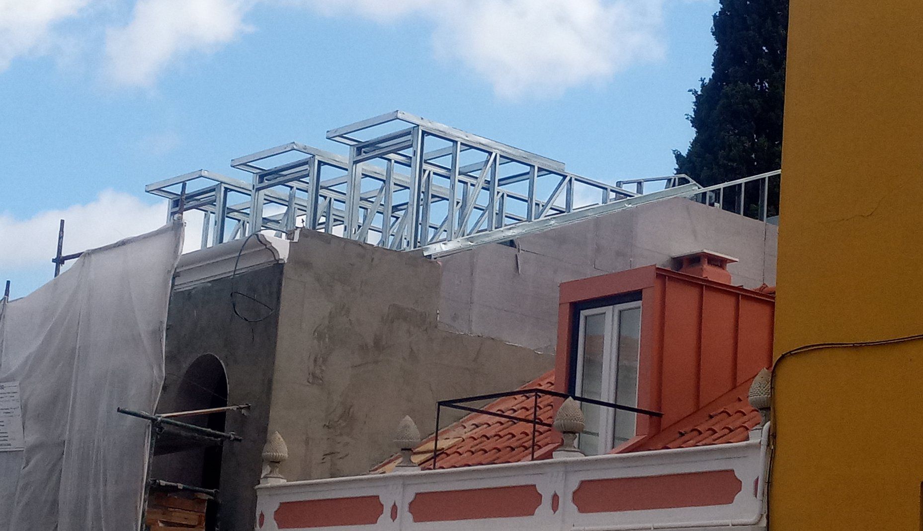 Construção de estrutura metálica no telhado de um edifício, com andaimes e cobertura parcial.