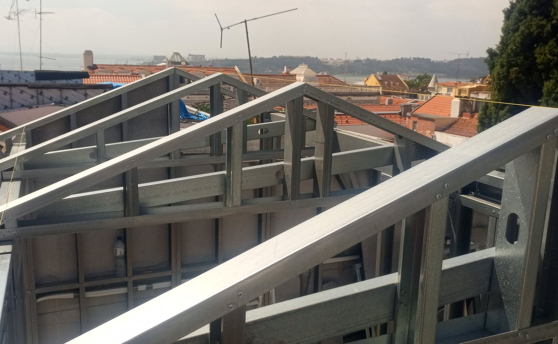 Estrutura metálica do telhado de um edifício, com prédios da cidade ao fundo.