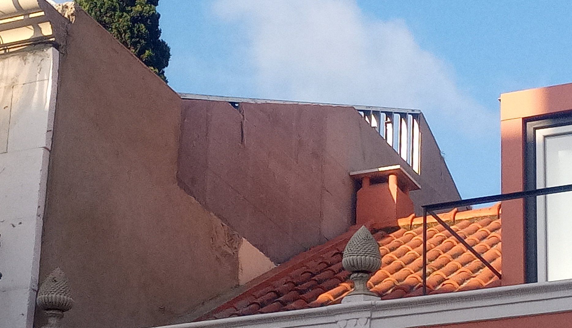 Prédios com telhados de telha vermelha e paredes cor de pêssego contra um céu azul.