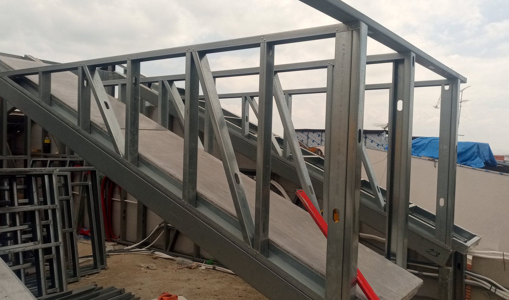 Estrutura metálica de escada em construção ao ar livre, cinza e prata, com suportes angulares.