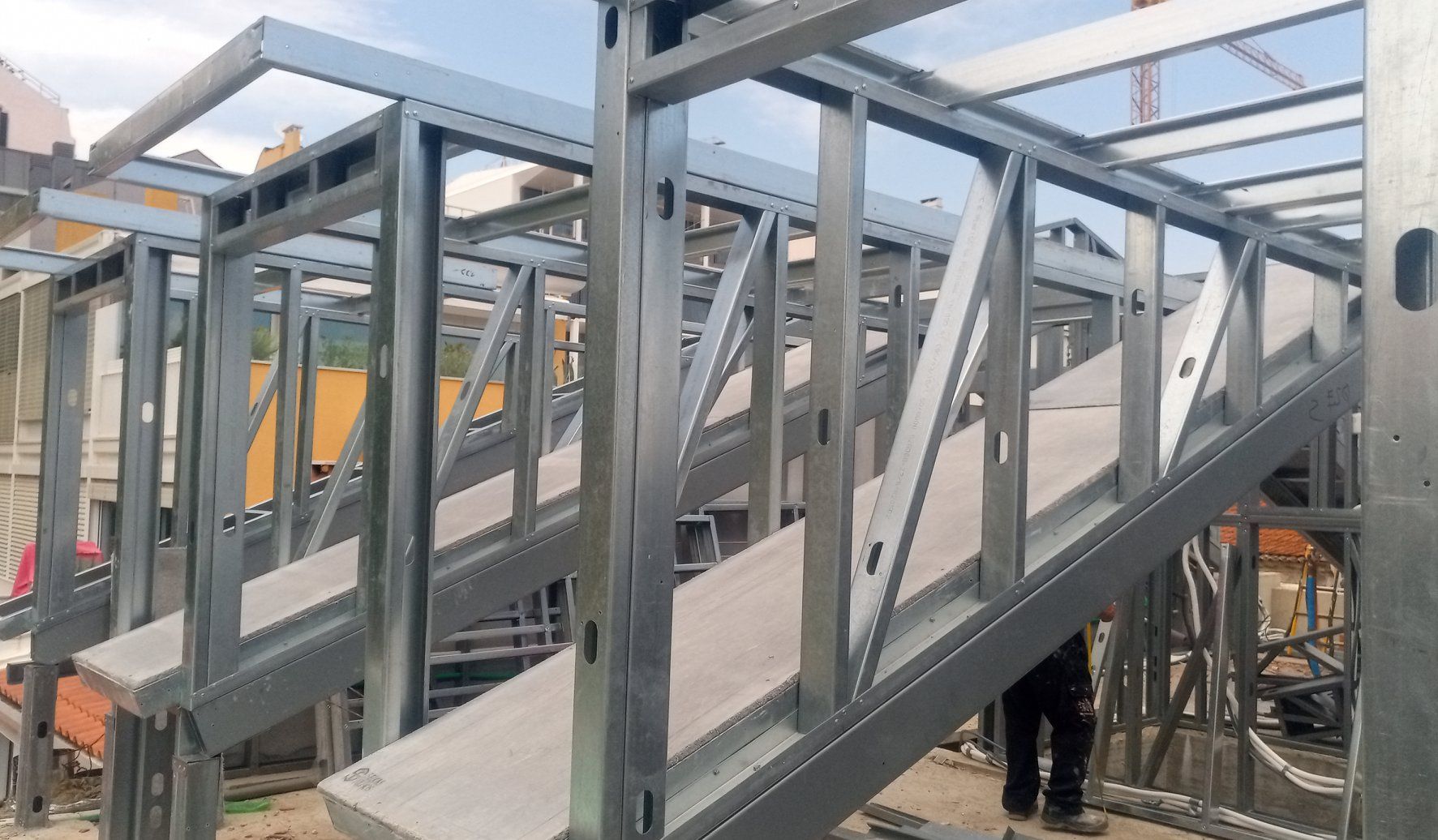 Estrutura metálica de uma escada em construção, ao ar livre, com suportes visíveis e degraus de concreto.