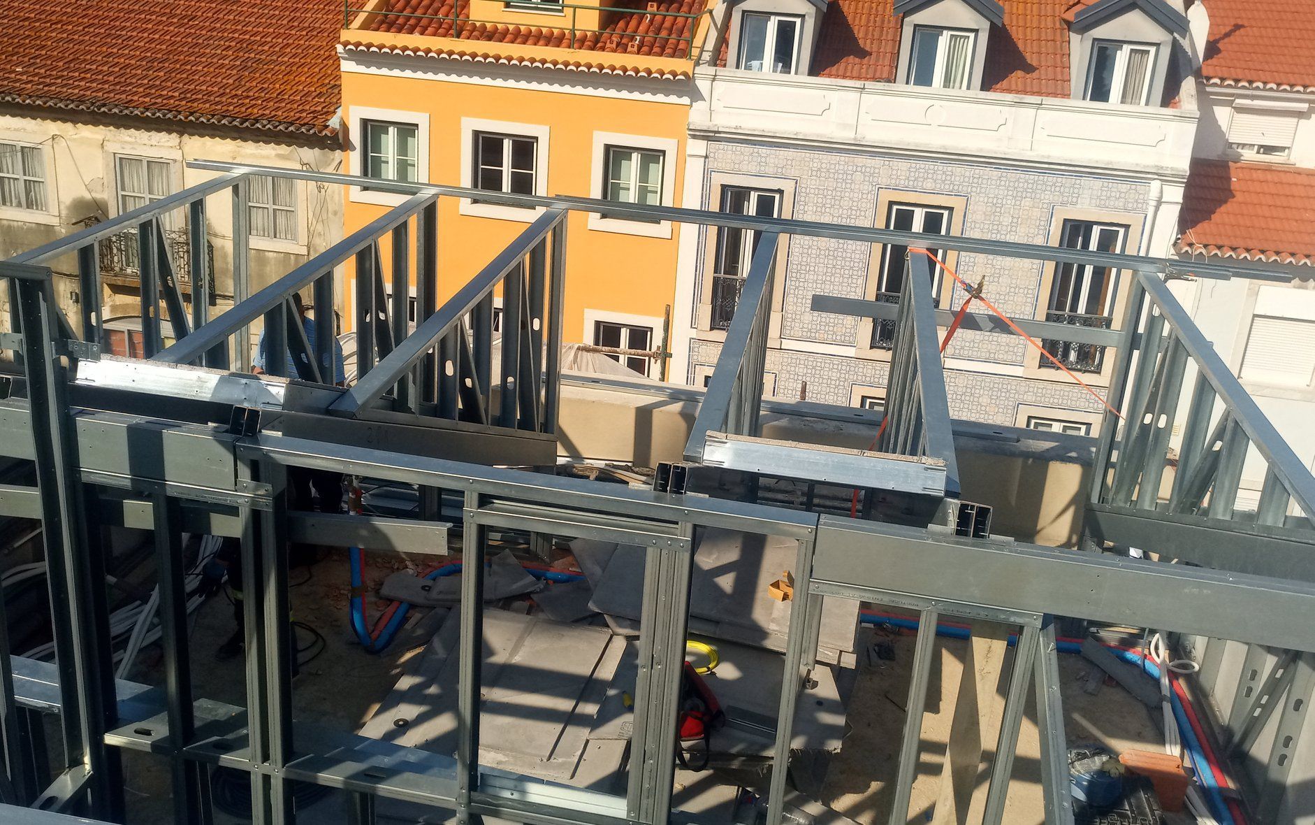 Estrutura metálica em construção, com vista para o telhado e edifícios coloridos ao fundo.