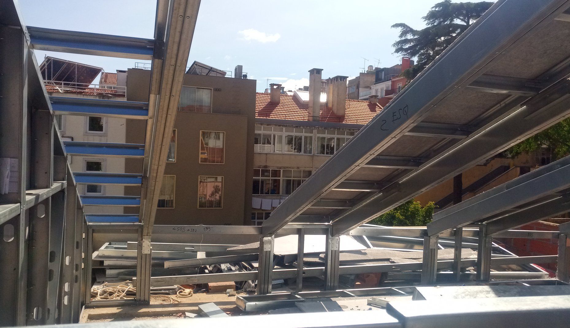 Construção com estrutura metálica tendo como pano de fundo a cidade, com seus prédios e telhados.