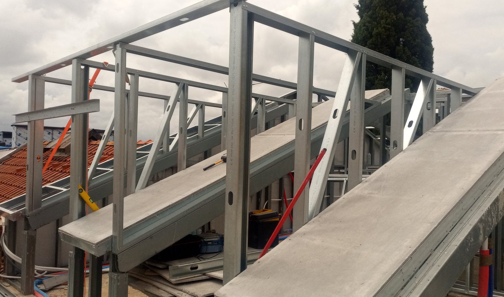 Estrutura de aço em construção no telhado com painéis de concreto e fiação elétrica exposta.