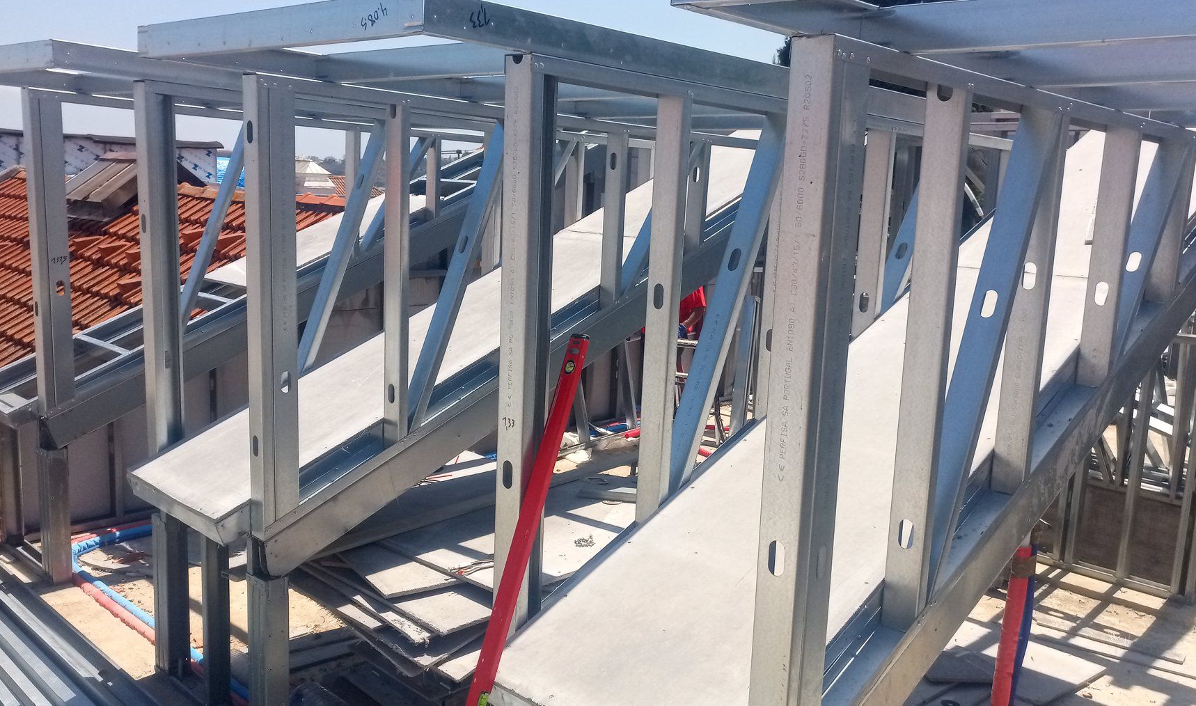 Estrutura metálica da escada interna de um edifício, com suportes, vigas e fiação elétrica vermelha visíveis.