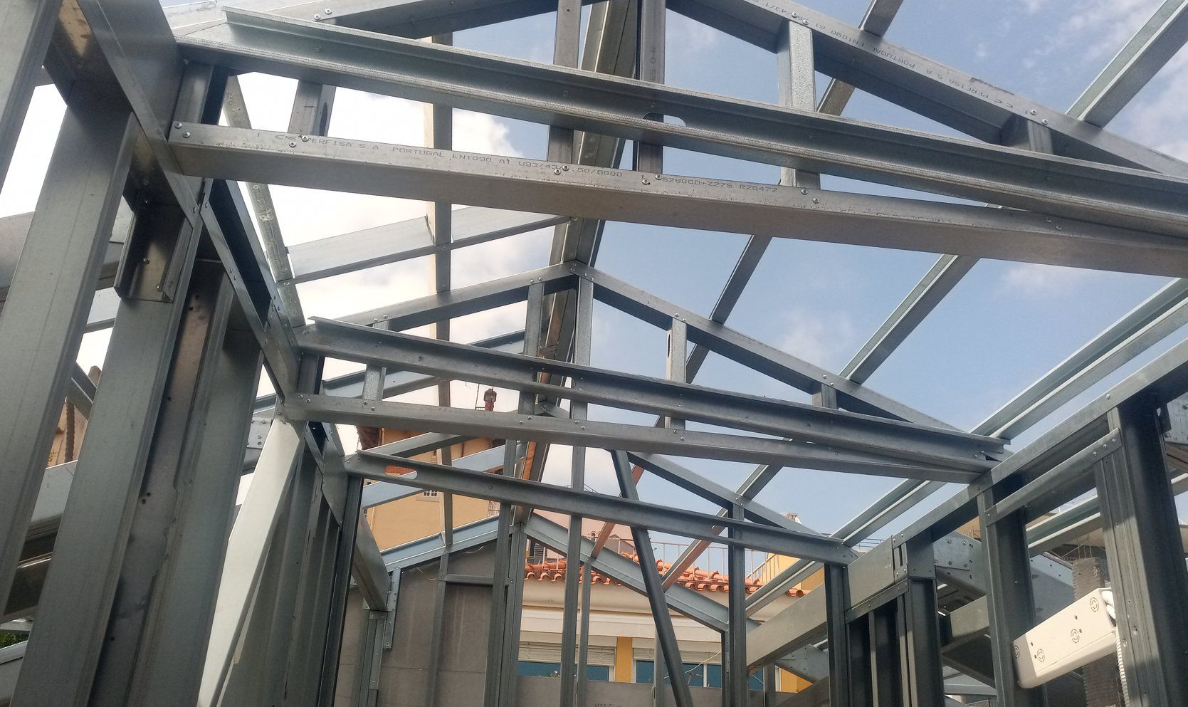 Estrutura metálica de um telhado e paredes em construção, sob um céu parcialmente nublado.