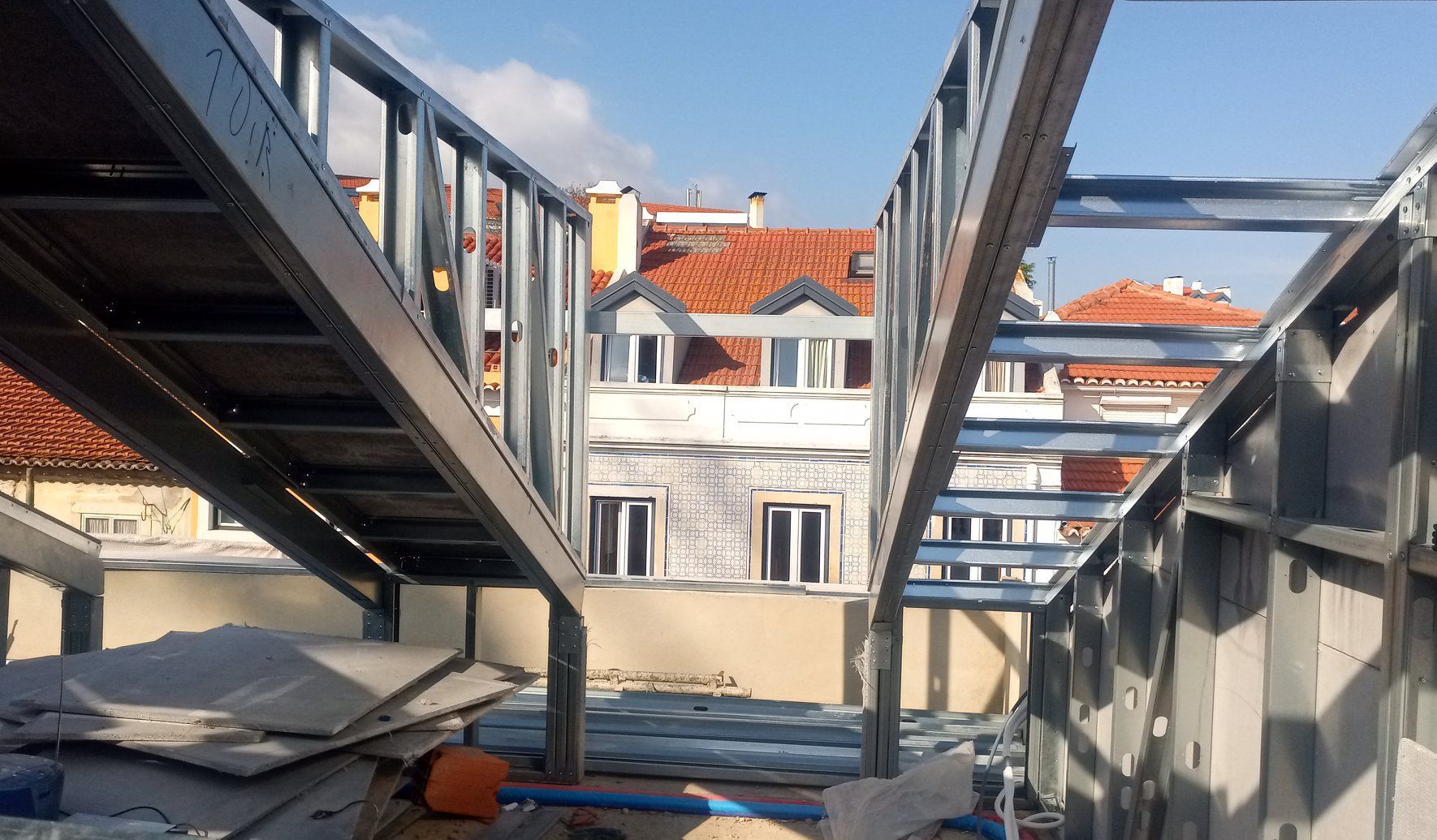 Estrutura metálica em um telhado, com prédios e céu azul ao fundo.