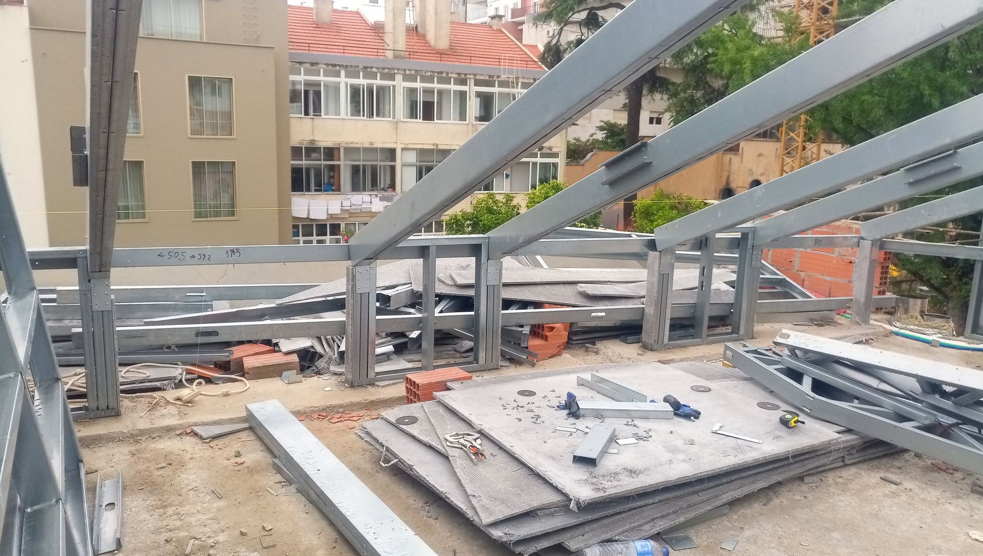 Estrutura de aço em um canteiro de obras no telhado, com prédios ao fundo.