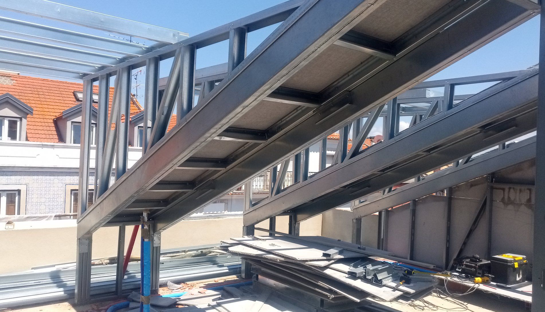 Estrutura metálica construída em um telhado, possivelmente uma passarela ou extensão, com céu limpo ao fundo.