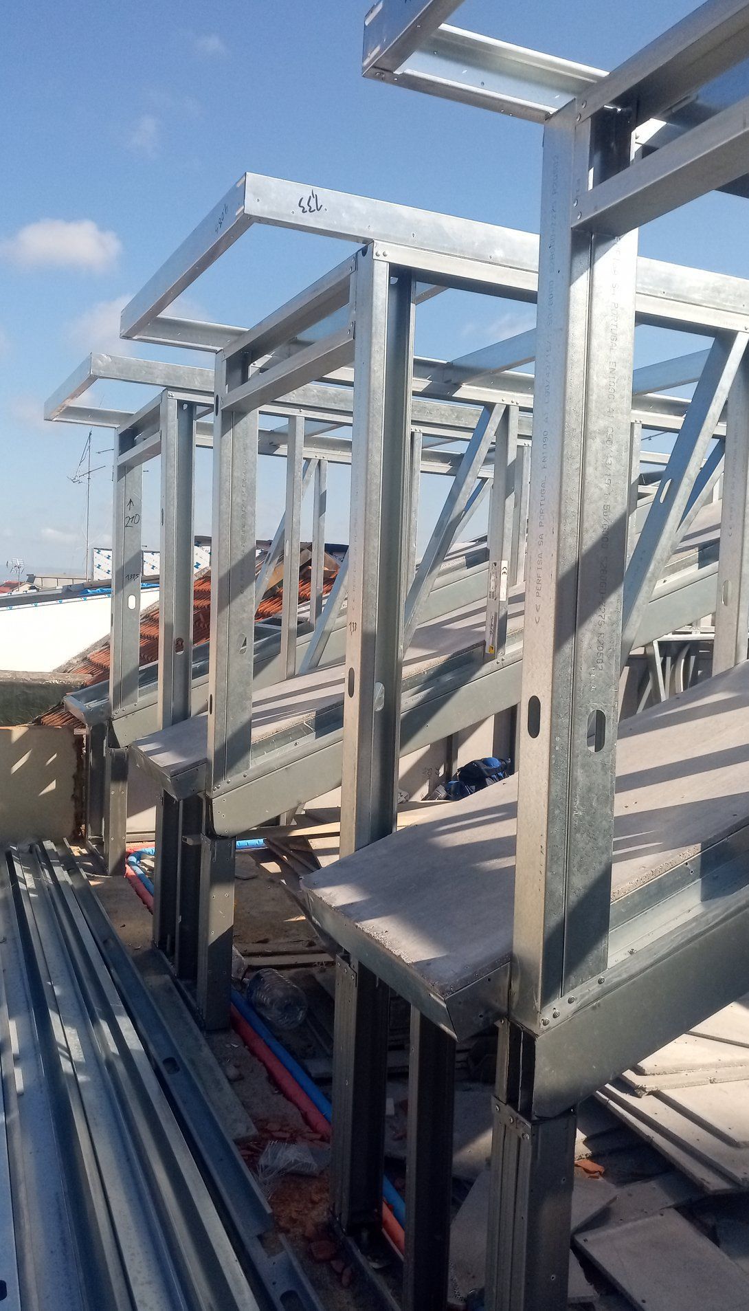 Estrutura de aço em um telhado com metal cinza e céu azul.