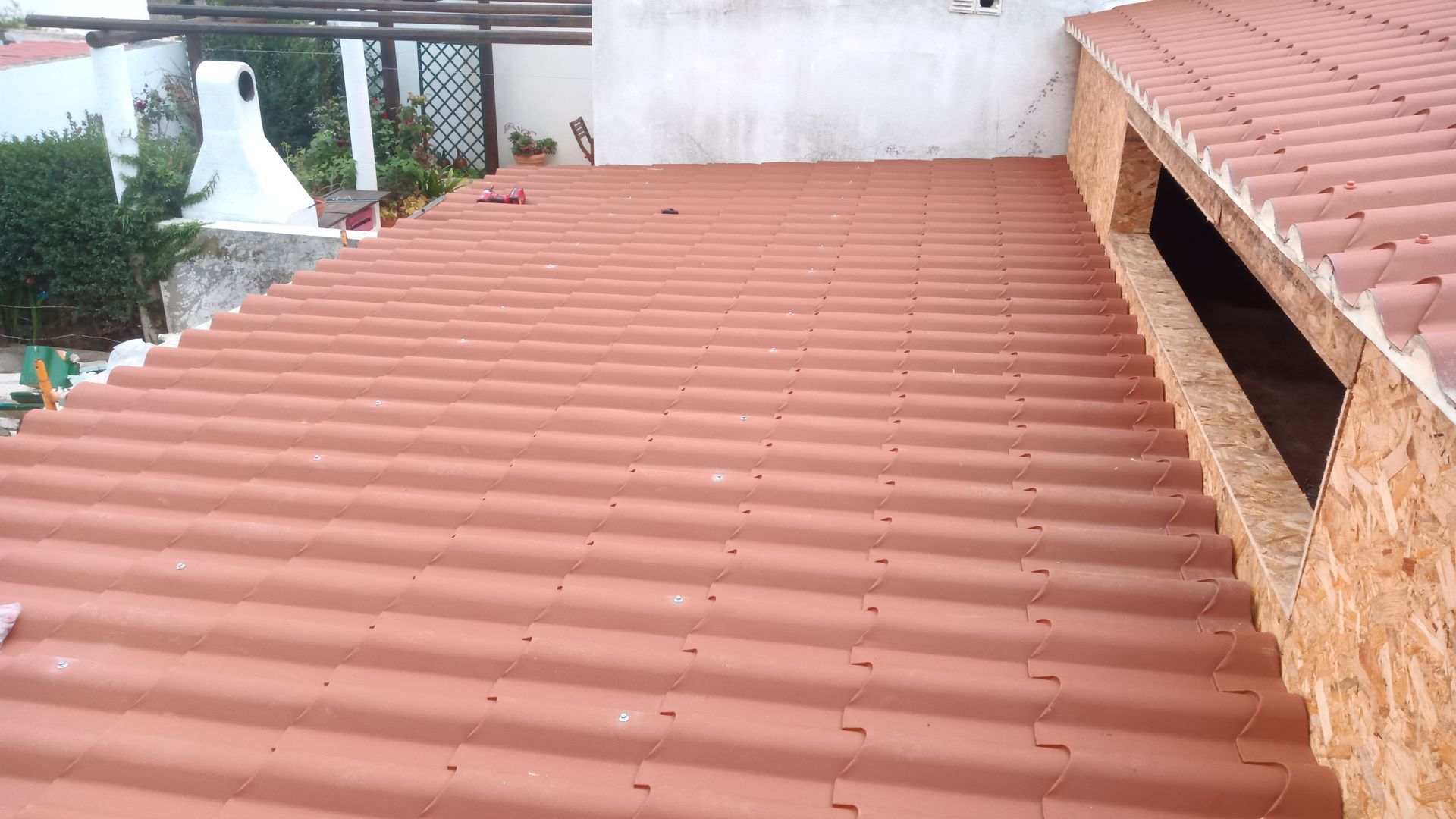 Telhado de telha vermelha em um edifício parcialmente aberto para o céu, com alvenaria aparente.