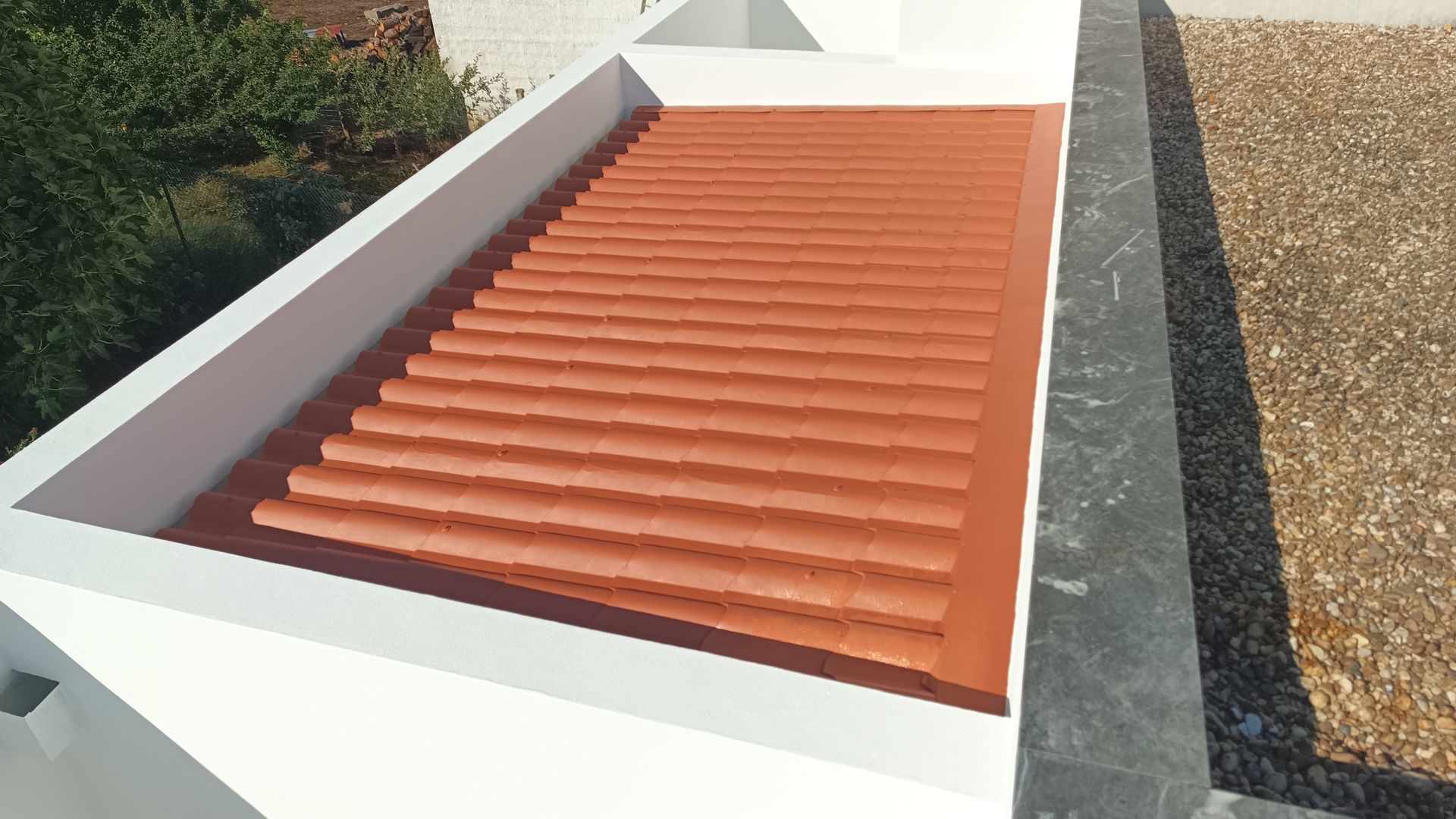 Vista de um telhado plano com telhas onduladas cor de terracota em meio a paredes brancas.