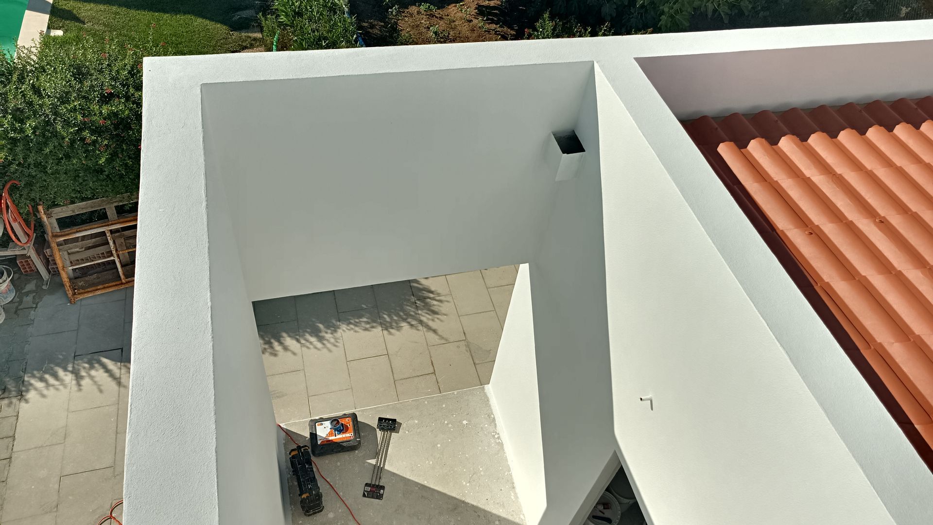 Vista aérea de um pátio com paredes brancas, telhado de telhas vermelhas e um dispositivo robótico sobre o piso pavimentado.