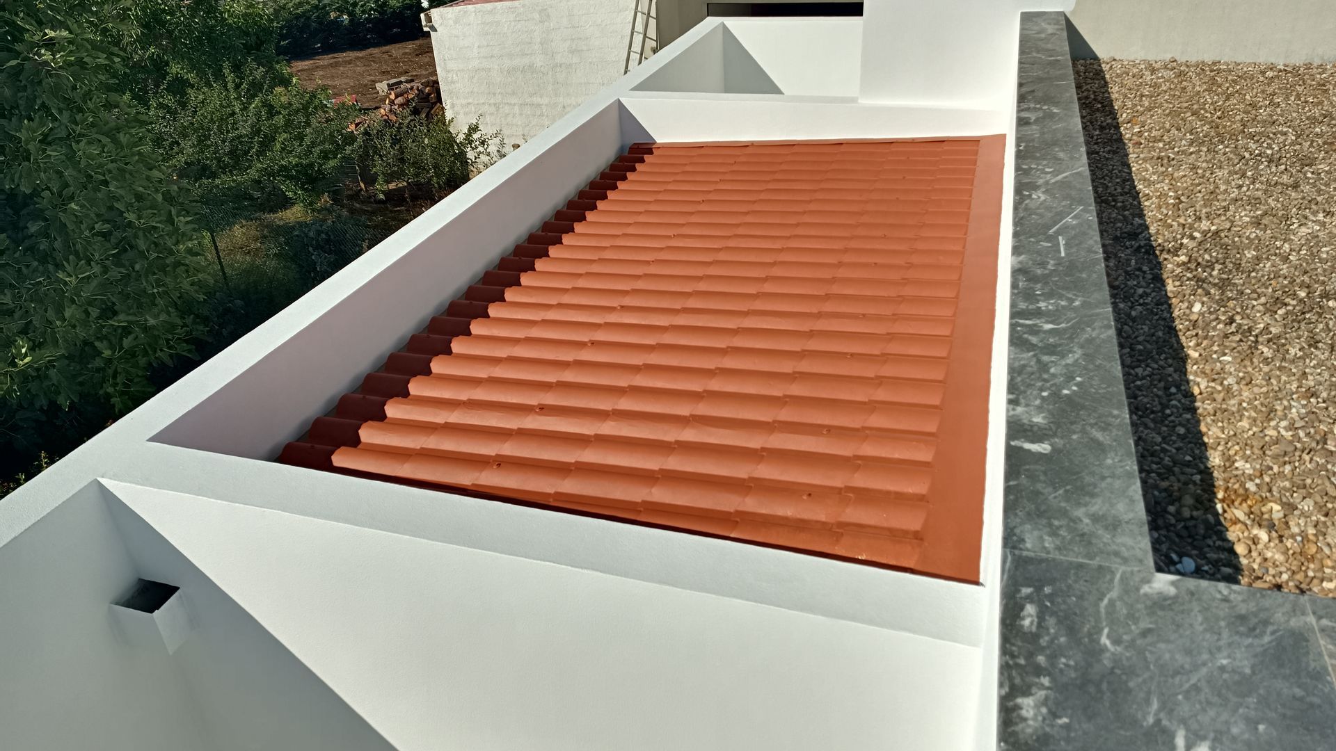Telhado de zinco vermelho em um prédio branco, com uma área de cascalho à direita.