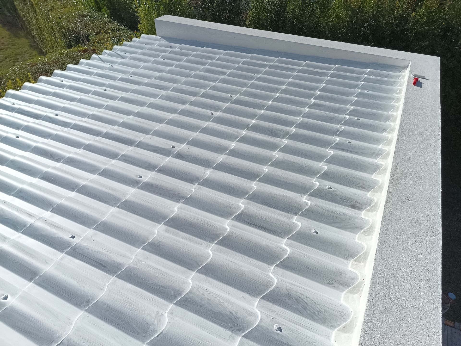 Telhado de zinco branco sobre uma estrutura de concreto, visto de cima, com vegetação ao fundo.