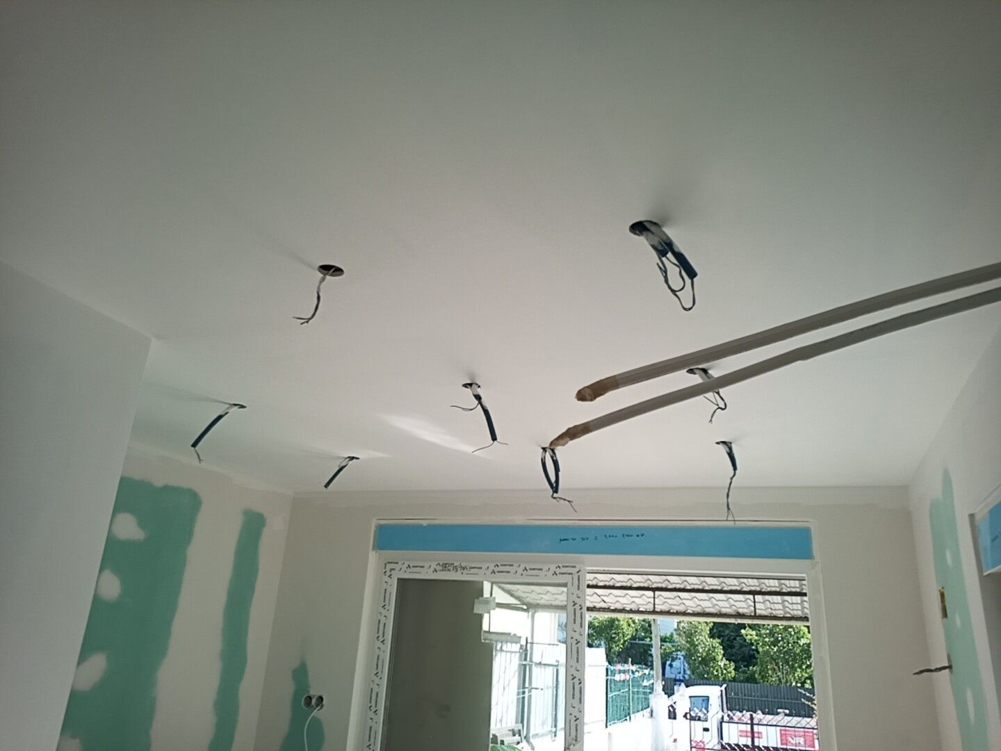 Interior do cômodo com fiação elétrica exposta pendurada no teto; parte das paredes de gesso acartonado já instalada.