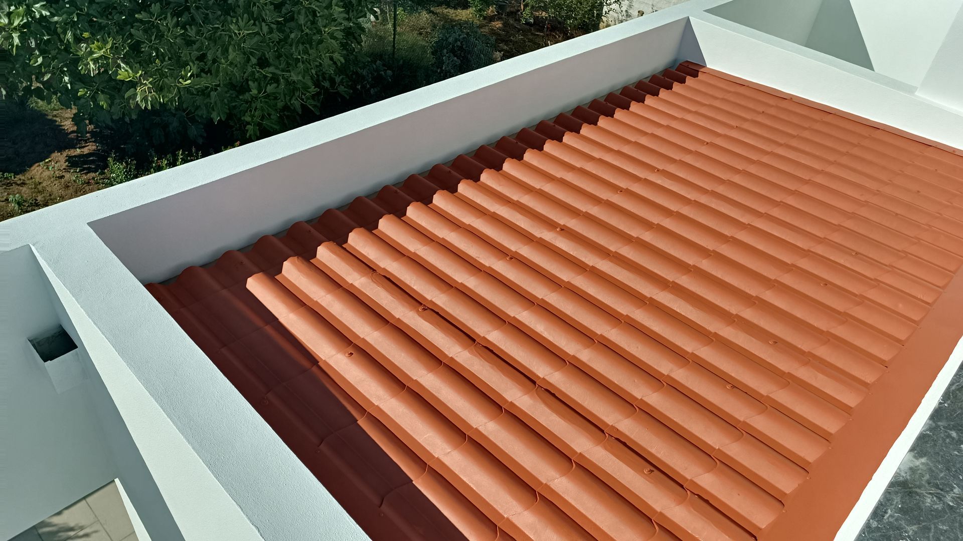 Vista aérea de um telhado plano de zinco ondulado, na cor laranja, cercado por paredes brancas.