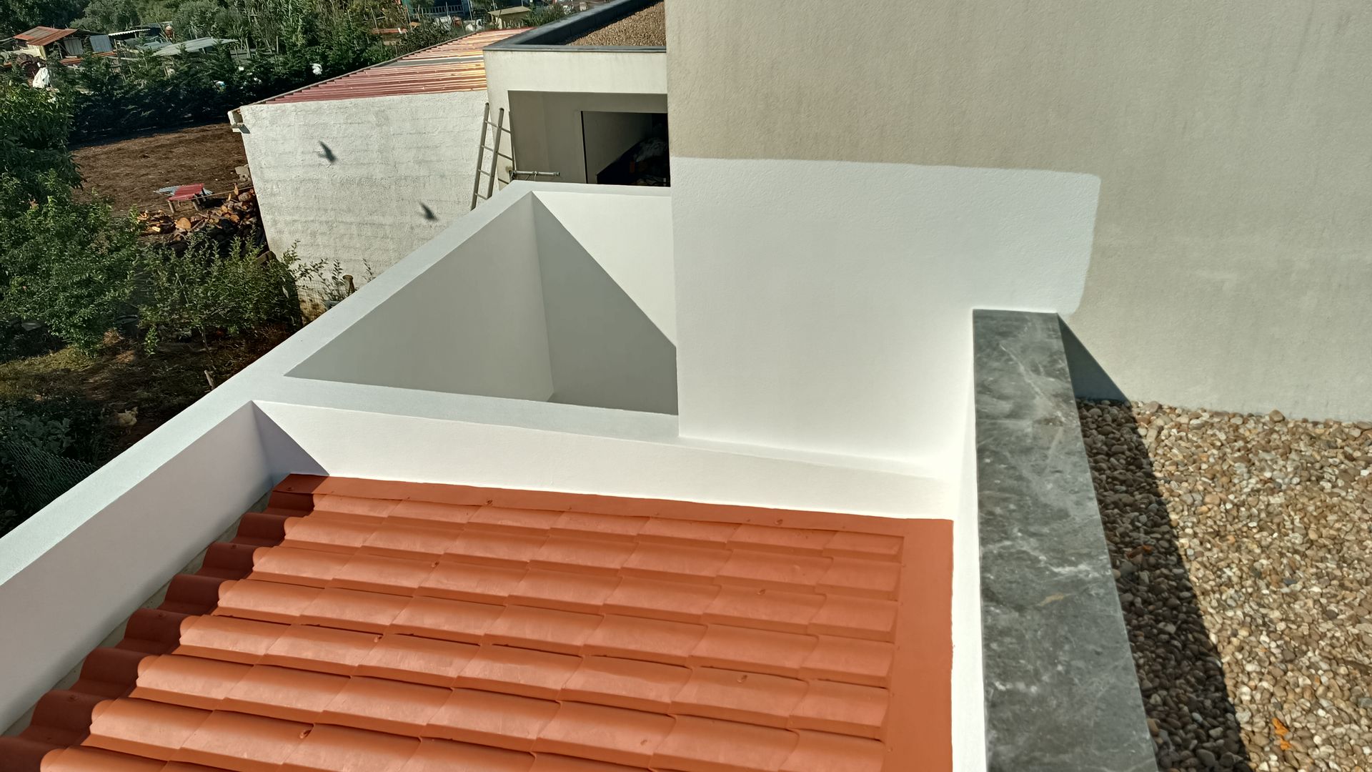 Telhas de terracota com paredes brancas e borda de pedra cinza, luz solar.
