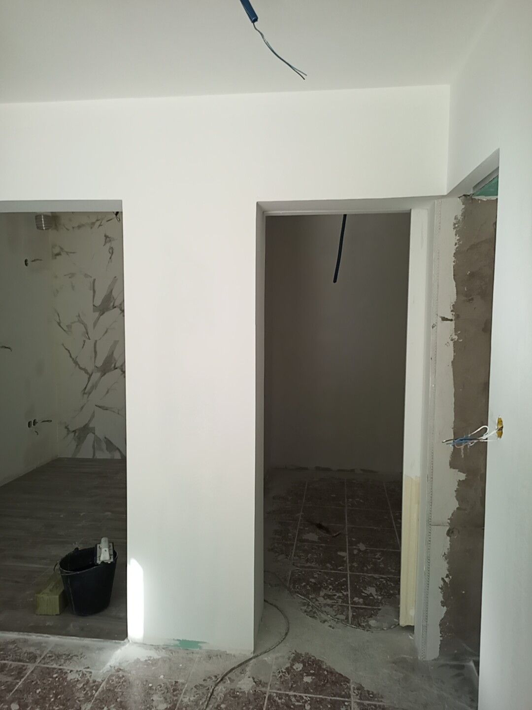 Vista interior de uma sala com duas portas, paredes brancas recém-pintadas e materiais de construção expostos.