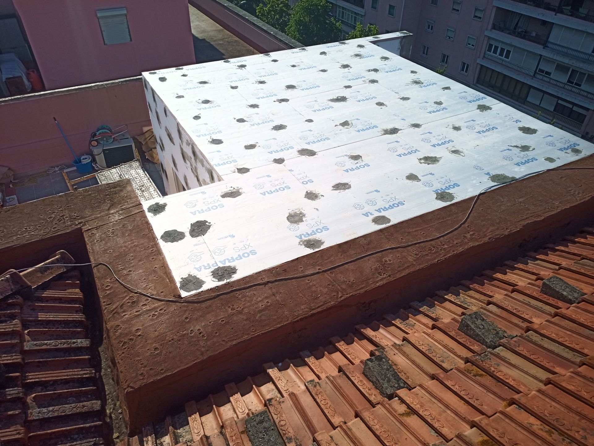 Projeto de isolamento de telhado: painéis brancos cobrem um telhado plano, com telhas vermelhas emoldurando-o.