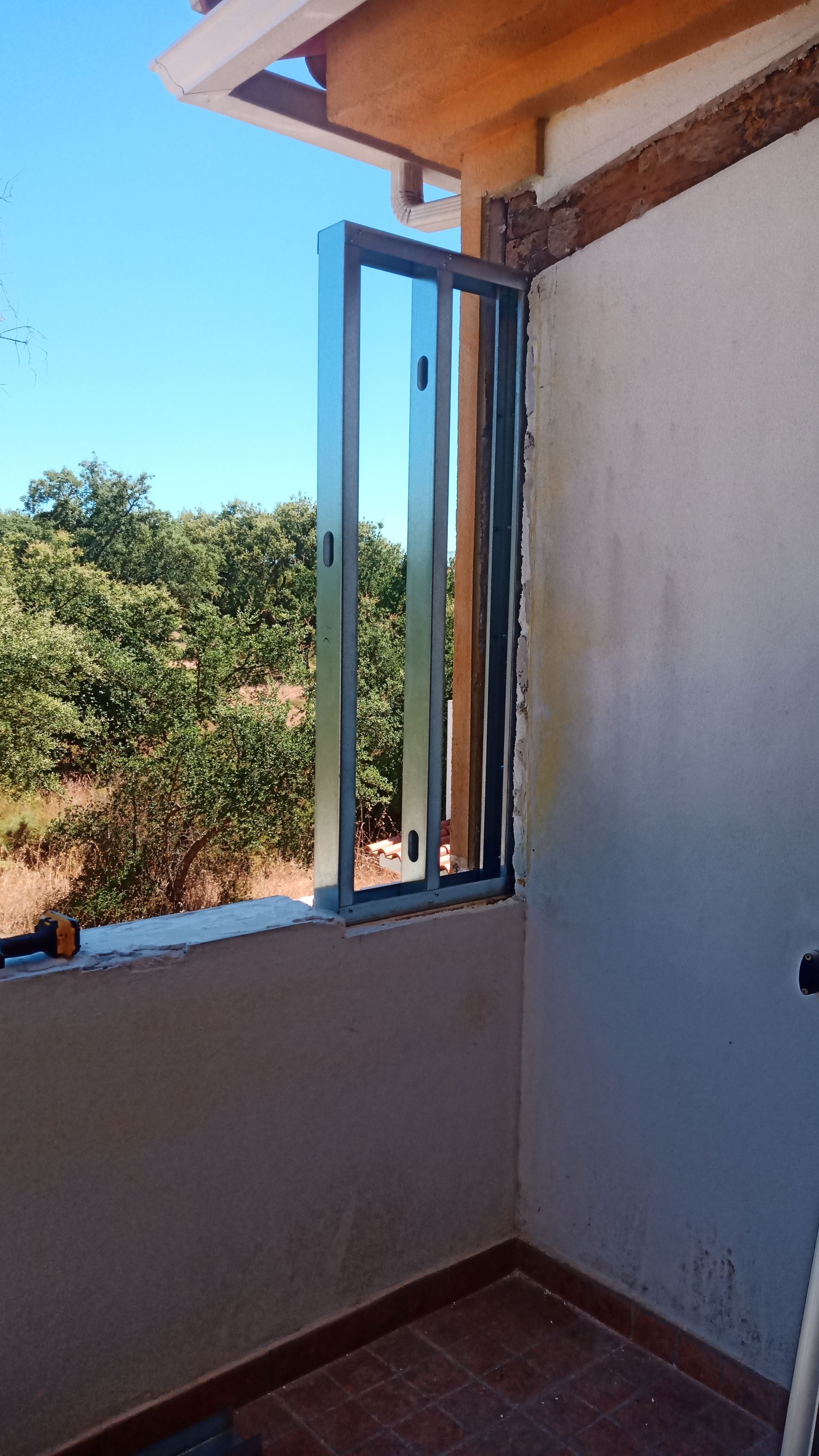 Uma janela deslizante parcialmente aberta em uma varanda com vista para as árvores contra um céu azul.