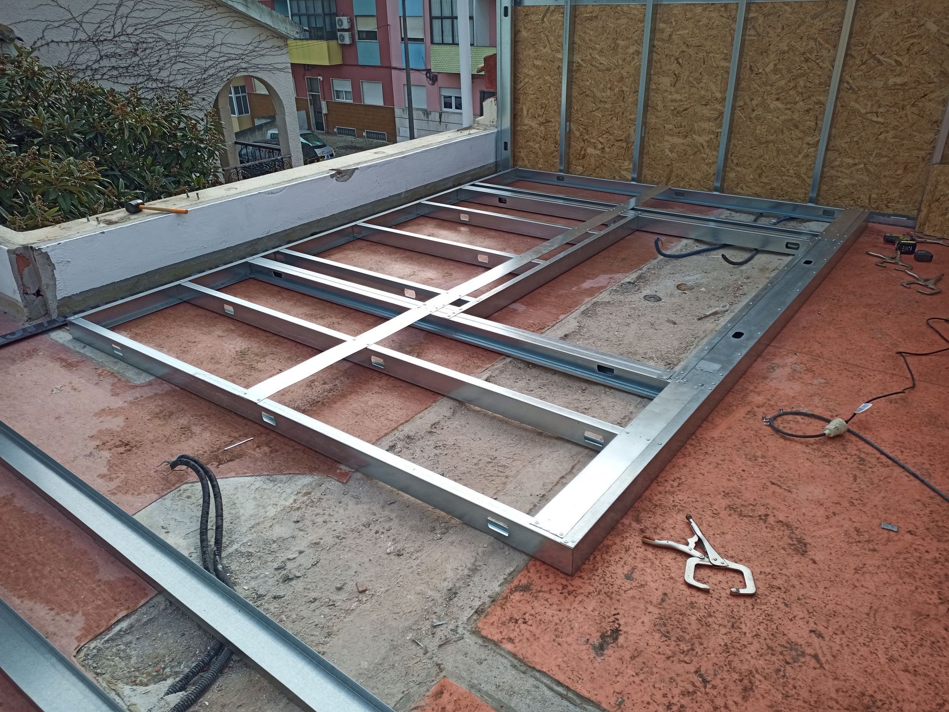 Estrutura metálica sendo construída ao ar livre sobre uma superfície de ladrilhos vermelhos, possivelmente para uma porta ou janela.