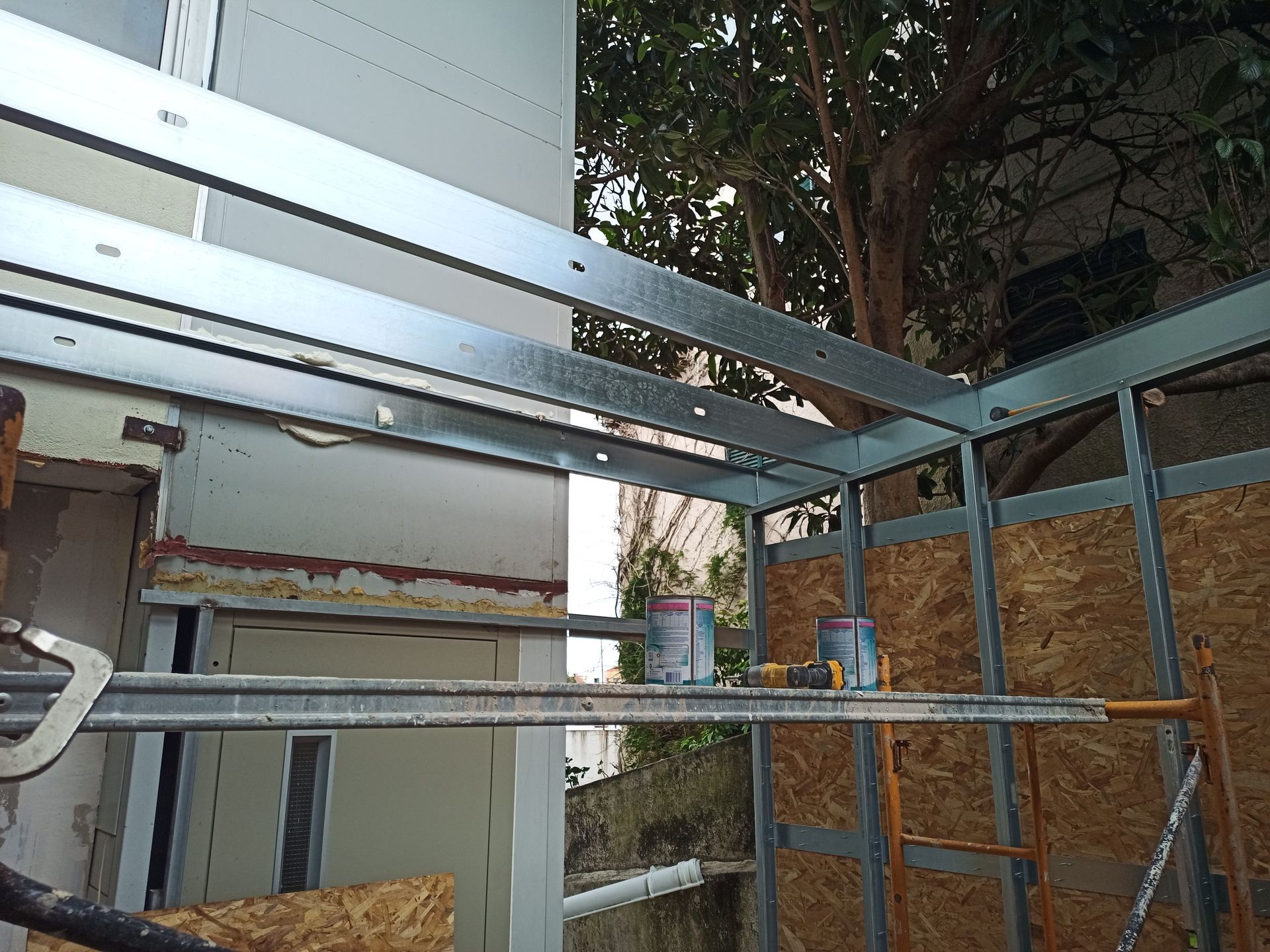 Estrutura metálica de uma construção em andamento; o revestimento de OSB é visível. Duas latas de tinta estão dentro da estrutura.