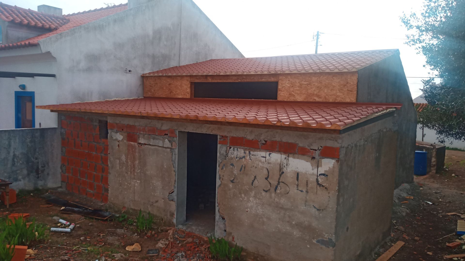 Prédio em construção com telhado de telha vermelha e paredes de concreto e tijolo.