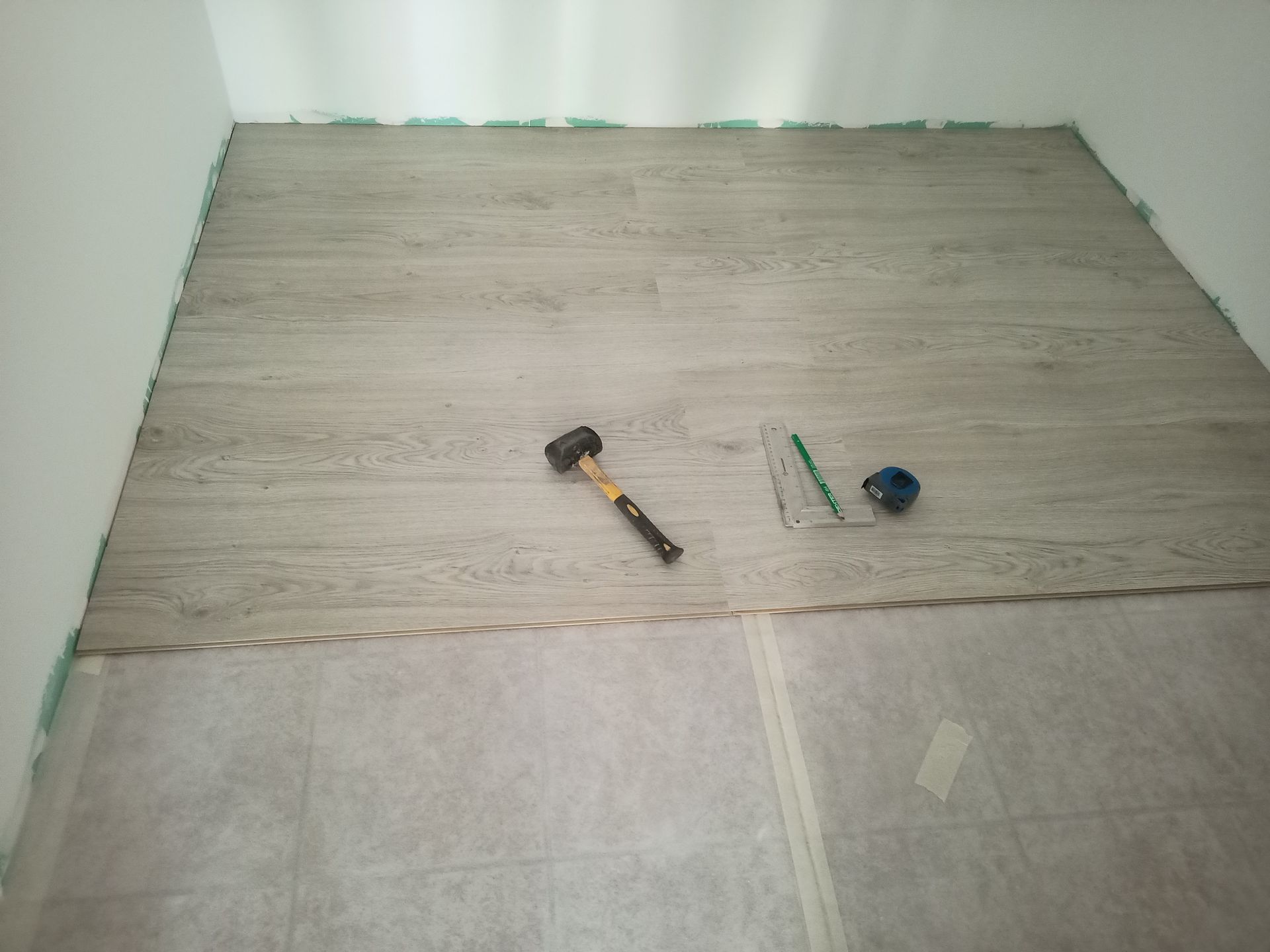 Instalando piso laminado em um cômodo. Martelo, lápis e outras ferramentas no piso novo.