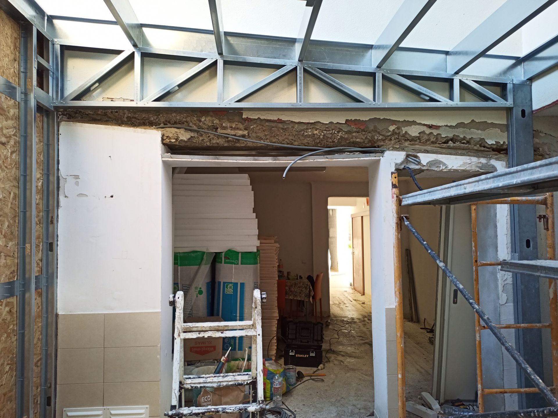 Canteiro de obras: abertura de porta, estrutura metálica, escada, parede parcialmente demolida.