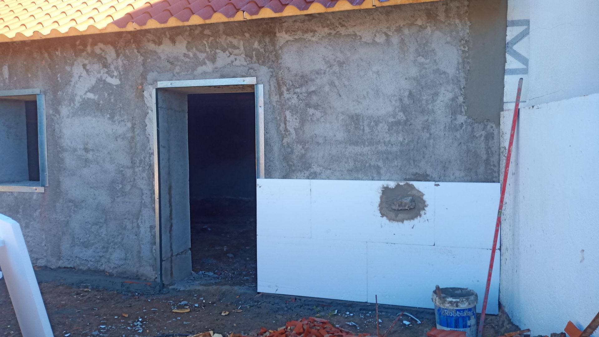 Exterior de um edifício em construção, com estuque e painéis de isolamento branco. Uma porta está aberta.
