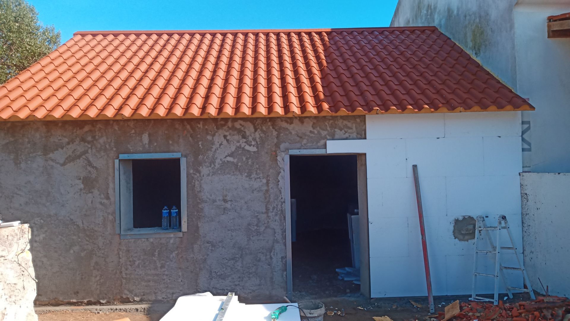 Prédio em construção com telhado de telha vermelha, parede de estuque inacabada e isolamento de espuma branca.