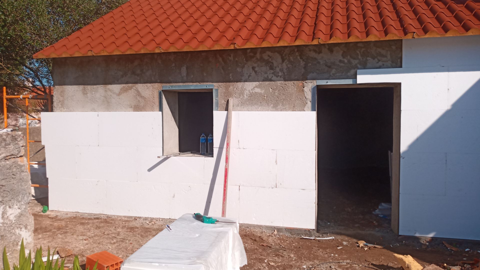 Exterior de um edifício em construção, com isolamento de espuma branca cobrindo parcialmente as paredes; telhado laranja.