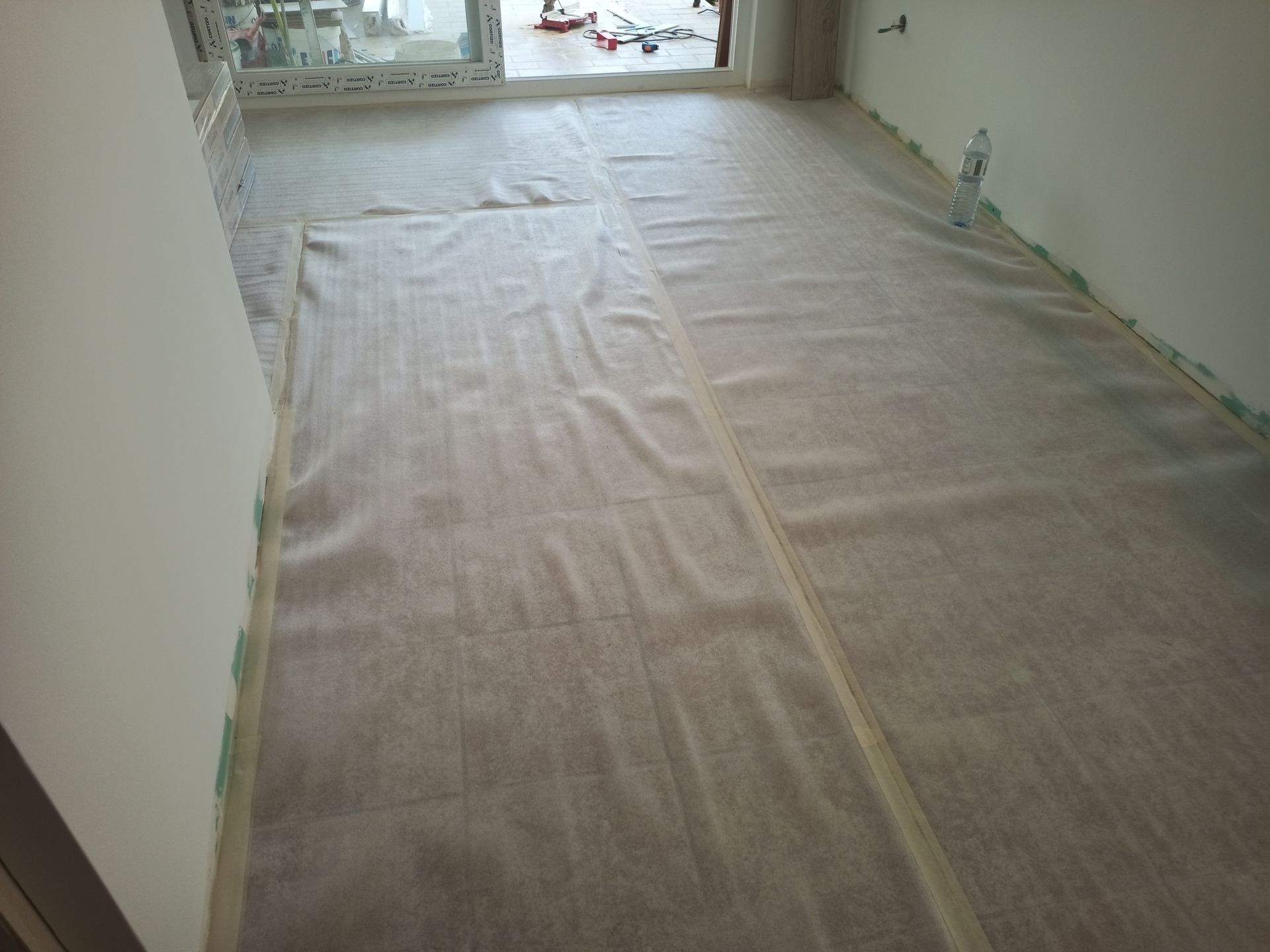 Quarto com piso coberto com papel protetor, próximo a uma janela e paredes.