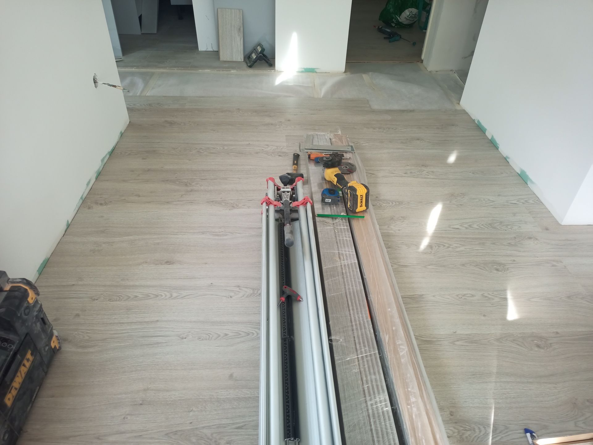 Um cômodo com piso de madeira clara, ferramentas e materiais de construção; paredes brancas.