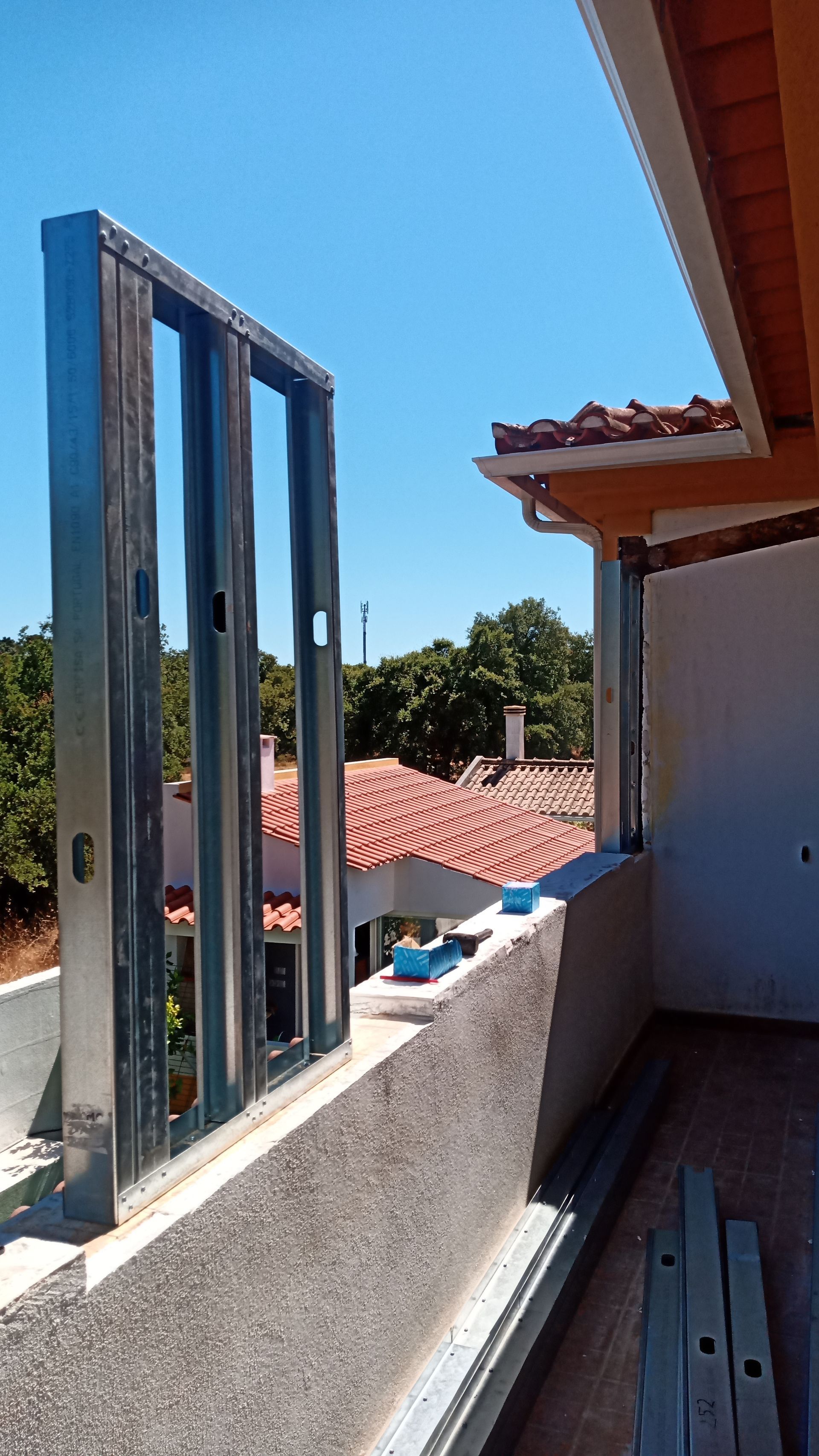 Estrutura metálica de uma parede em construção numa varanda com céu azul ao fundo.