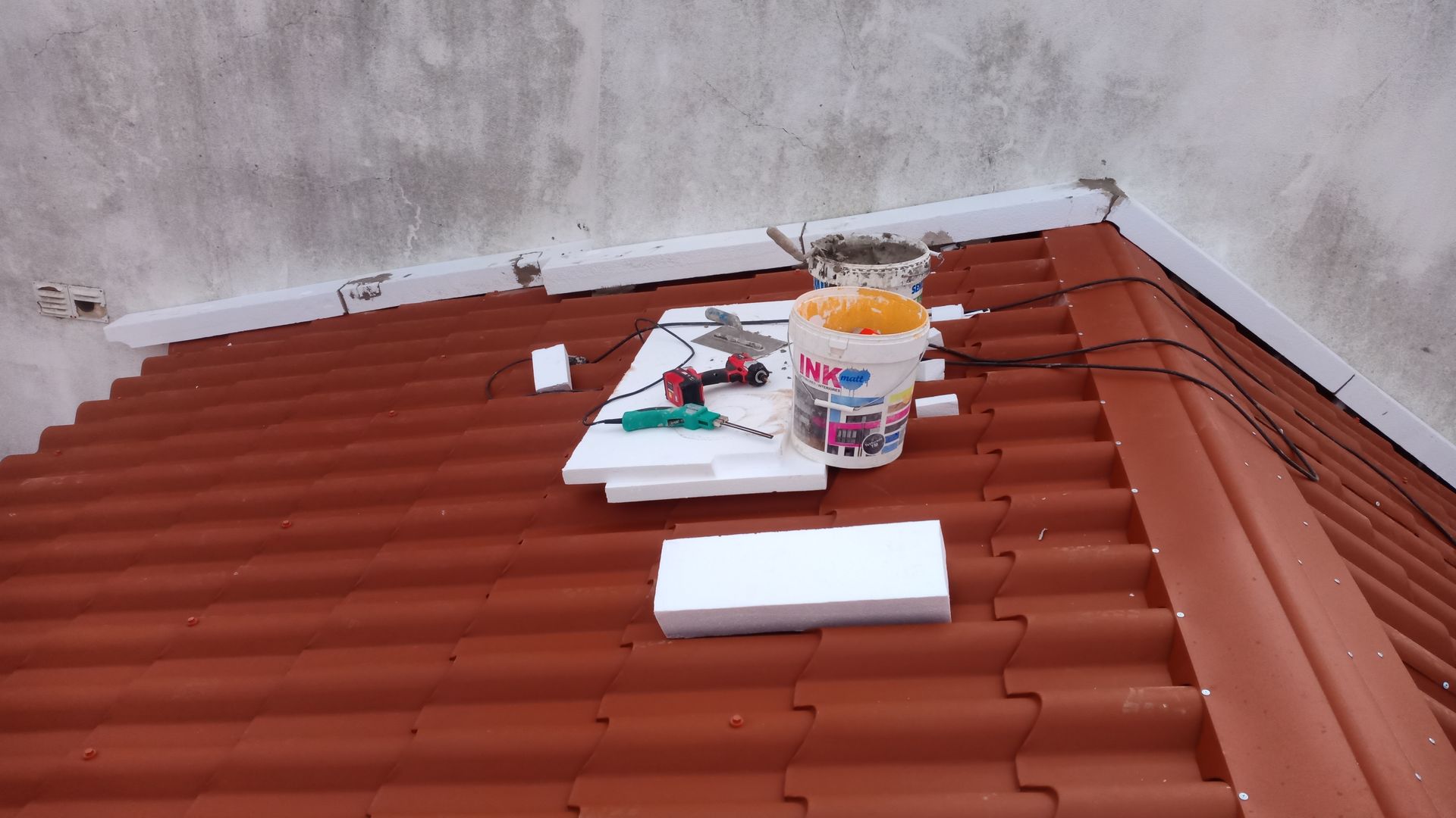 Telhado com ferramentas e materiais para reparo, incluindo isopor, balde e furadeira.