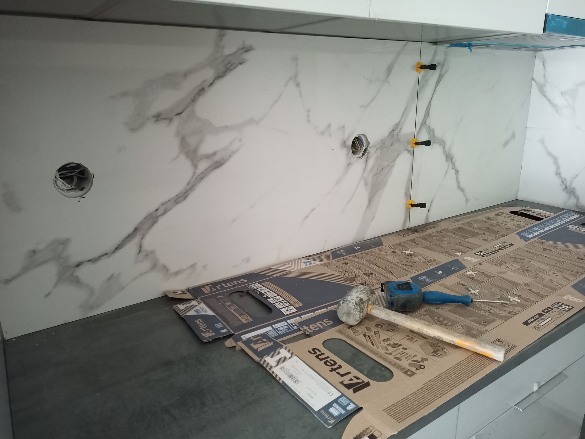 Revestimento de parede com azulejos estampados em mármore em construção, com ferramentas e espaçadores de nivelamento sobre a bancada.