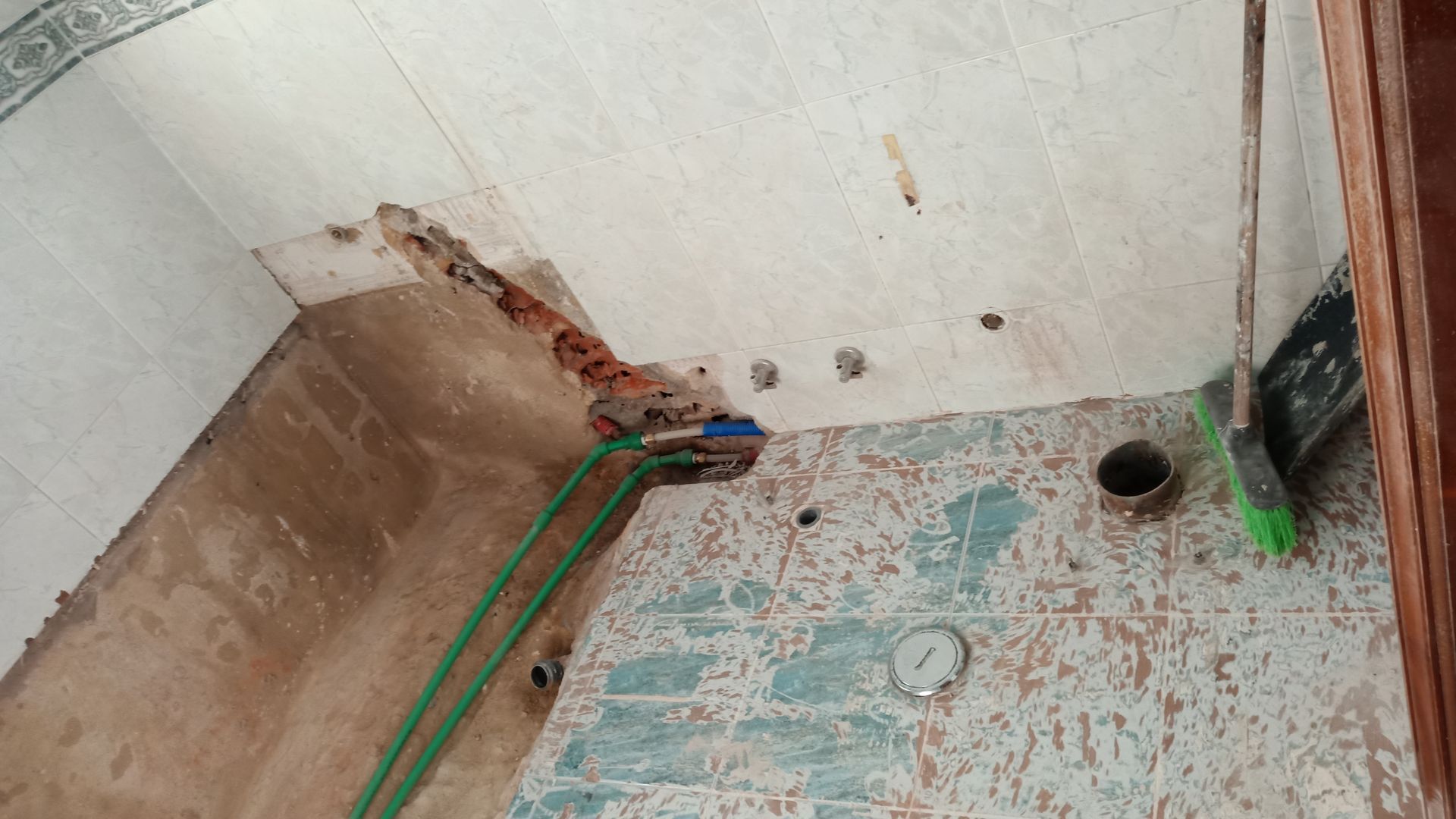 Interior de um canteiro de obras com fiação exposta e teto danificado. Fios verdes percorrem uma parede texturizada.