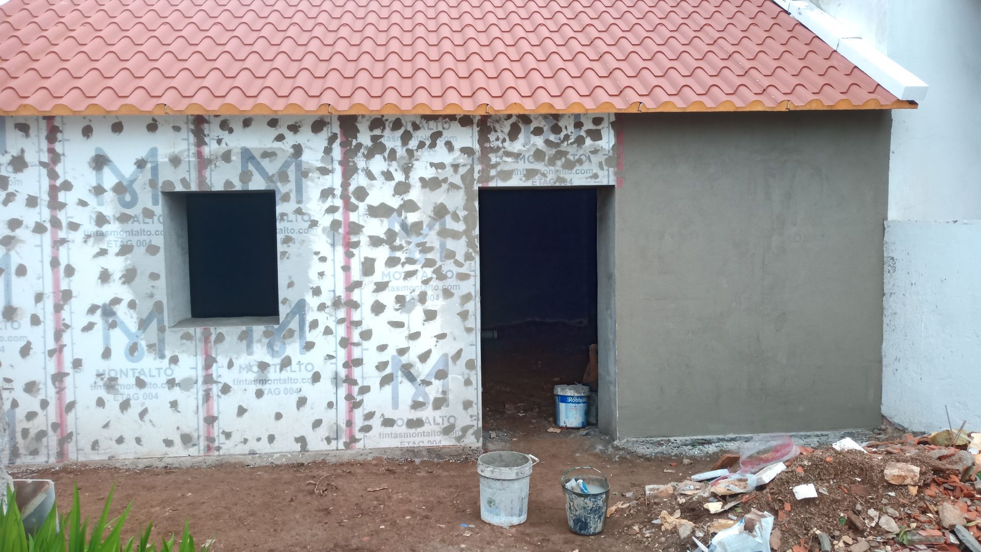 Exterior de um edifício em construção, mostrando uma janela, uma porta e paredes texturizadas.