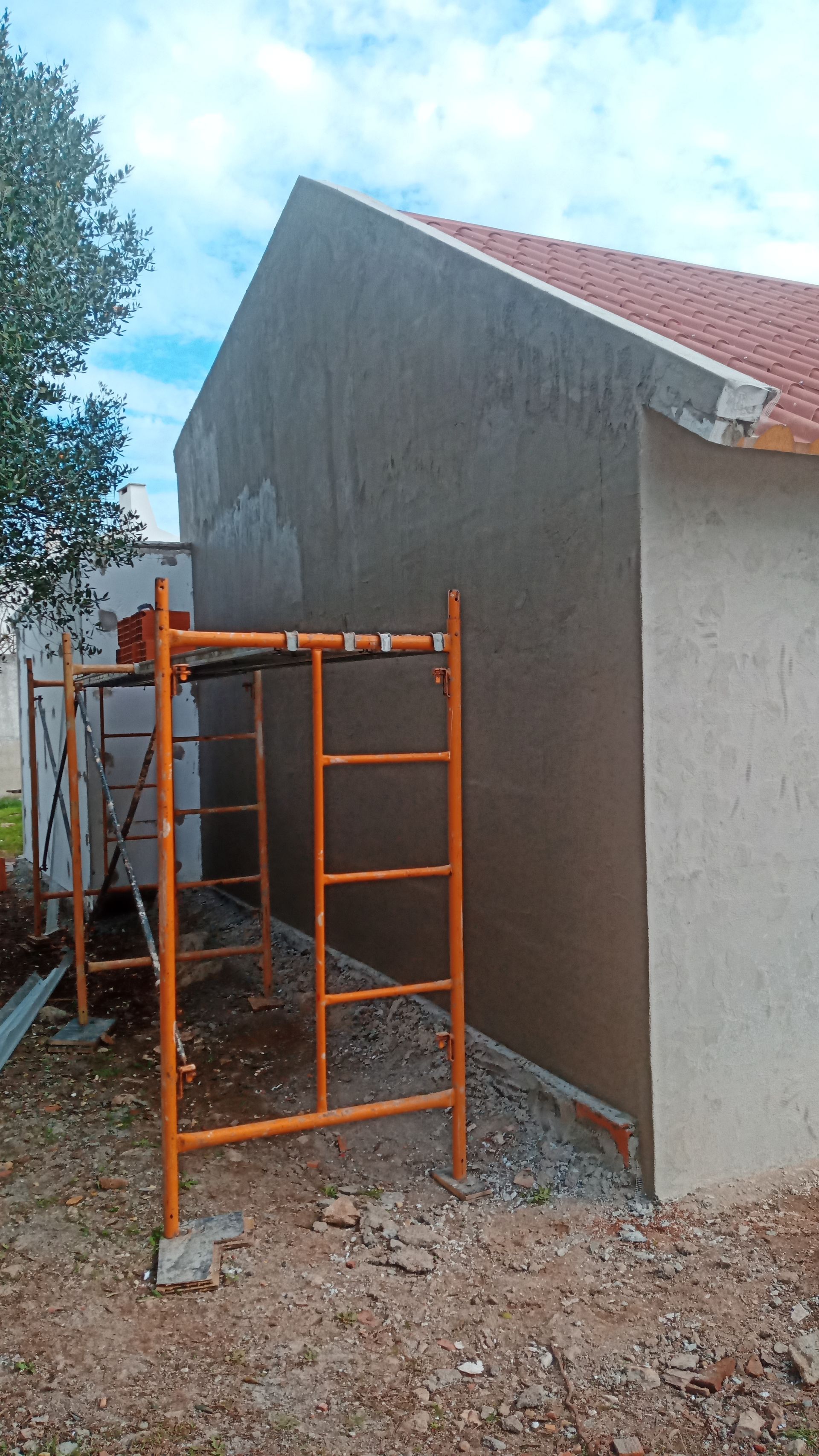 Andaimes de construção ao lado da parede de um edifício com acabamento em estuque, em tons de laranja e cinza, céu azul.